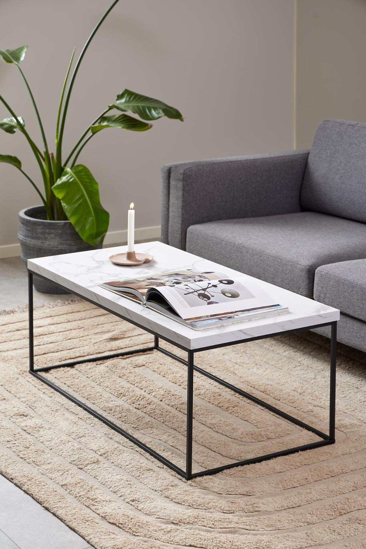Couchtisch Barossa mit weißer Marmorplatte und schwarzem Metallgestell, Blickwinkel leicht erhöht, mit Buch, Kerze und Pflanze auf der Tischplatte.