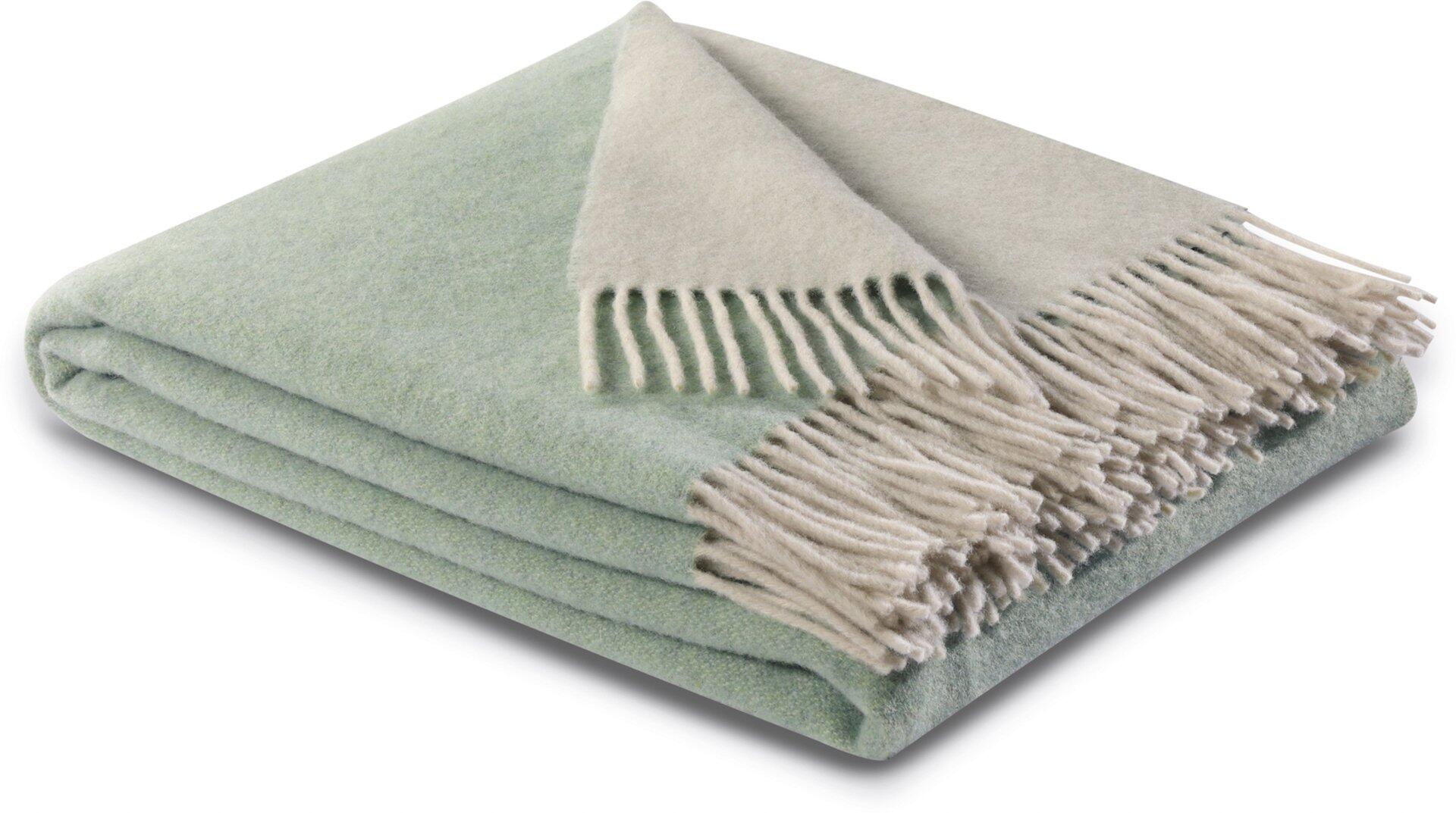 Cashmere-Plaid in salvia-creme mit Franse, drapiert über die Lehne eines Sessels, präsentiert die Textur und den warmen Farbton.