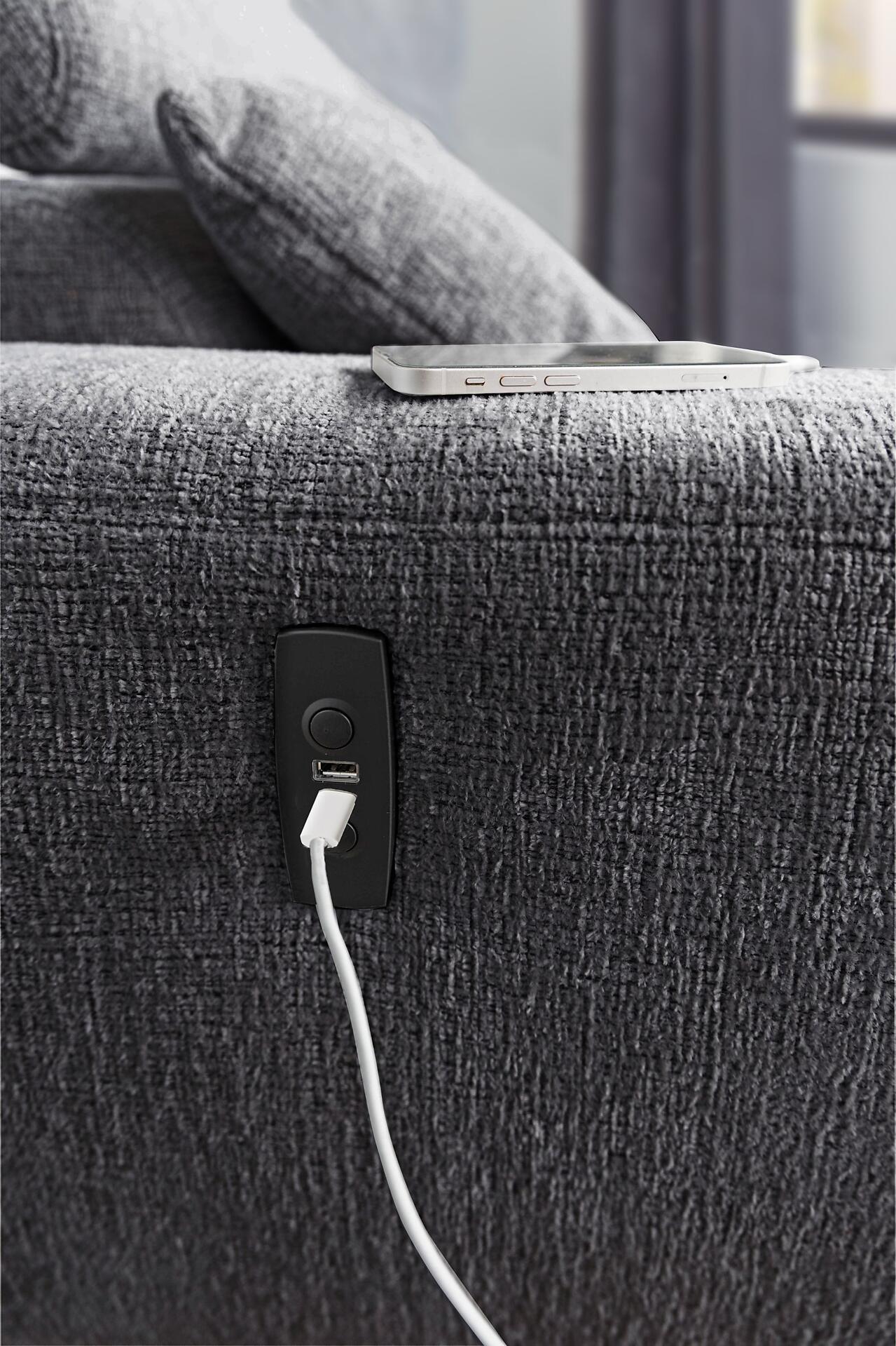 Wohnlandschaft Drifter: Detailaufnahme der Armlehne mit integriertem Steckdosenmodul für USB- und Stromanschluss, auf der ein Smartphone geladen wird.