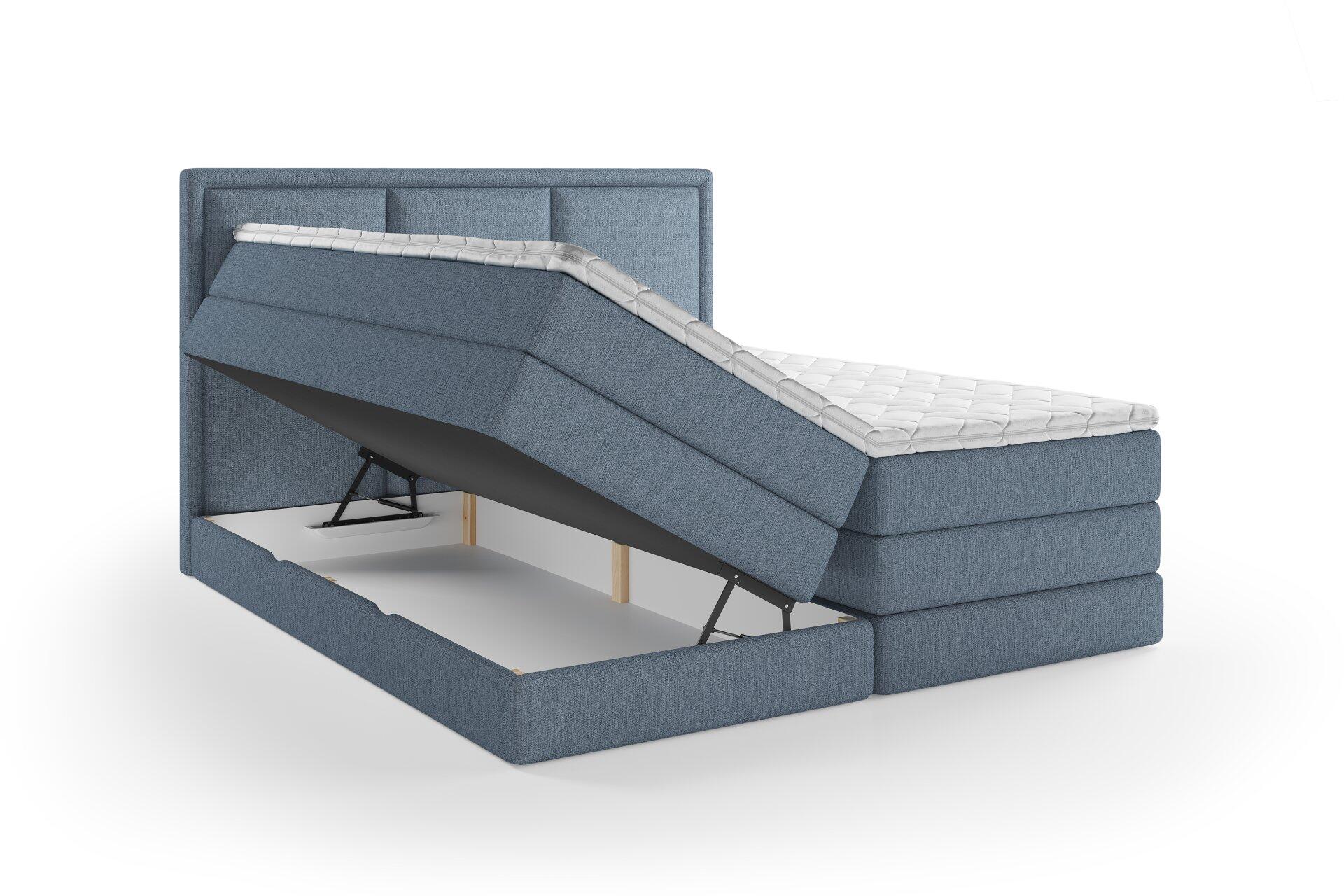 Blaues Boxspringbett Swing mit hochgestepptem Kopfteil und aufgeklapptem Bettrahmen, der Stauraum durch Gasdruckfedern freigibt.