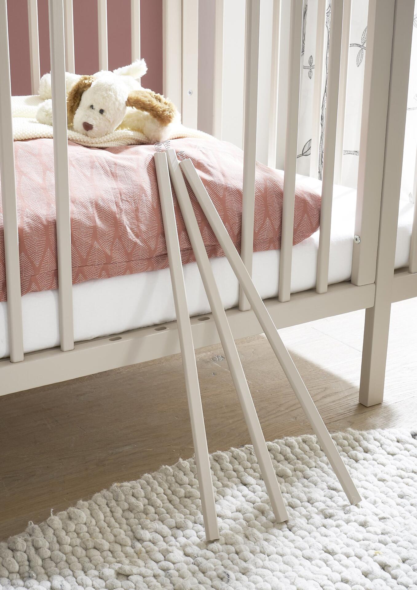 Babybett Peppini mit ausgefahrener Sicherheitsabsenkung und Bettlaken mit roséfarbenem Muster.