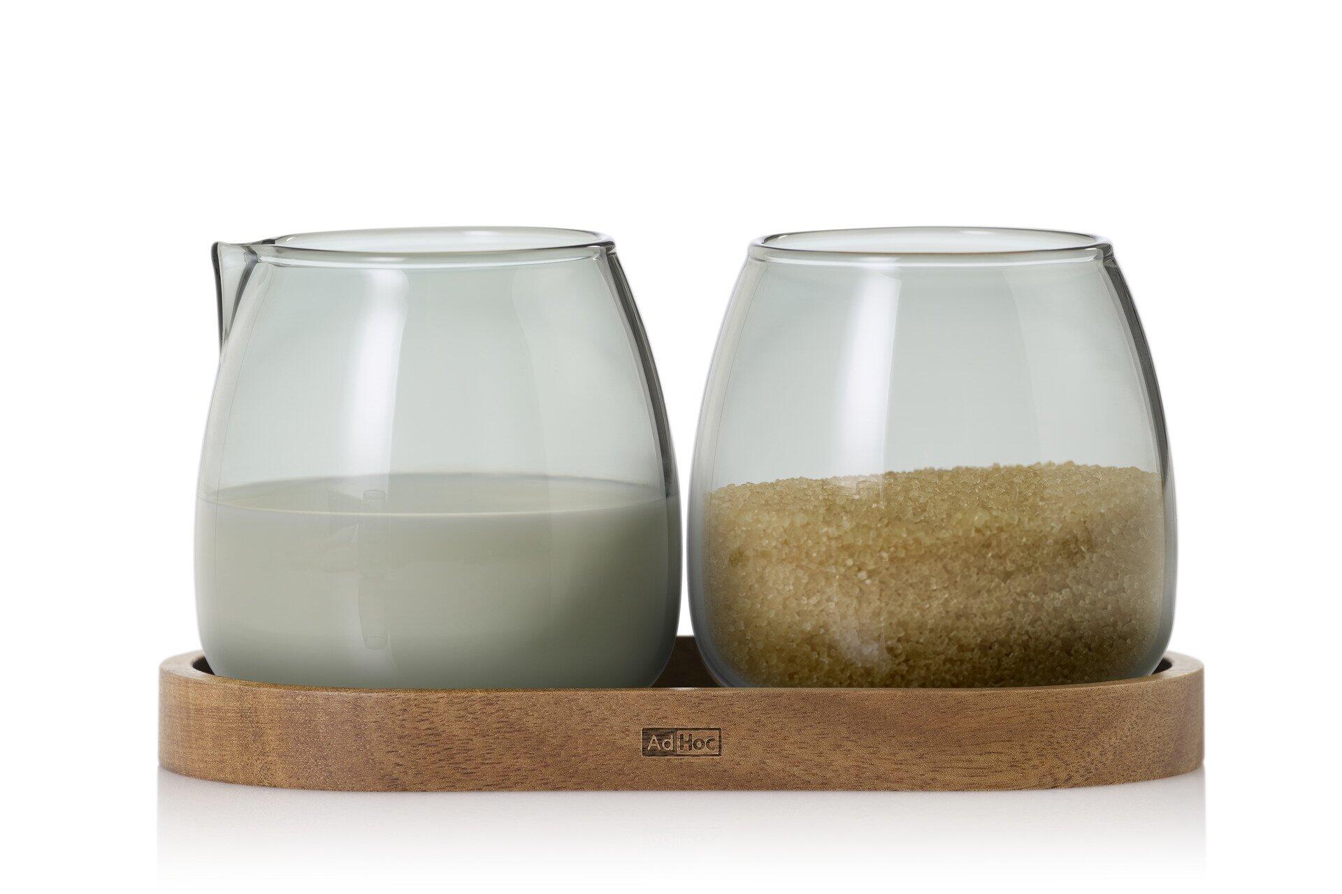 Milch- und Zucker Set Yuna mit zwei Glasbehältern in konischer Form auf einem Holztablett mit leicht erhöhtem Rand, gefüllt mit Milch und braunem Zucker.