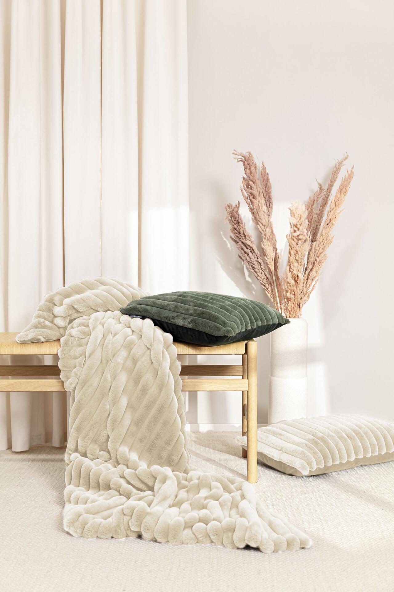 Kissenhülle Raya mit Fellstreifen-Design, liegend auf einer Bank zwischen weiteren Kissen und dekoriert mit getrockneten Halmen.