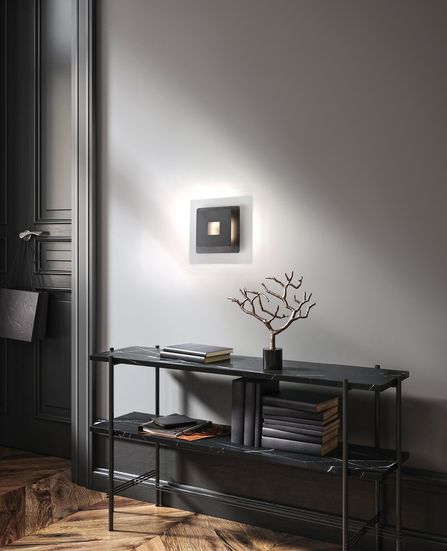 Schwarze Wandleuchte Hennes mit quadratischem Design und integriertem LED-Leuchtmittel an einer grauen Wand, im Fokus zusammen mit einem Tisch mit Marmorplatte.