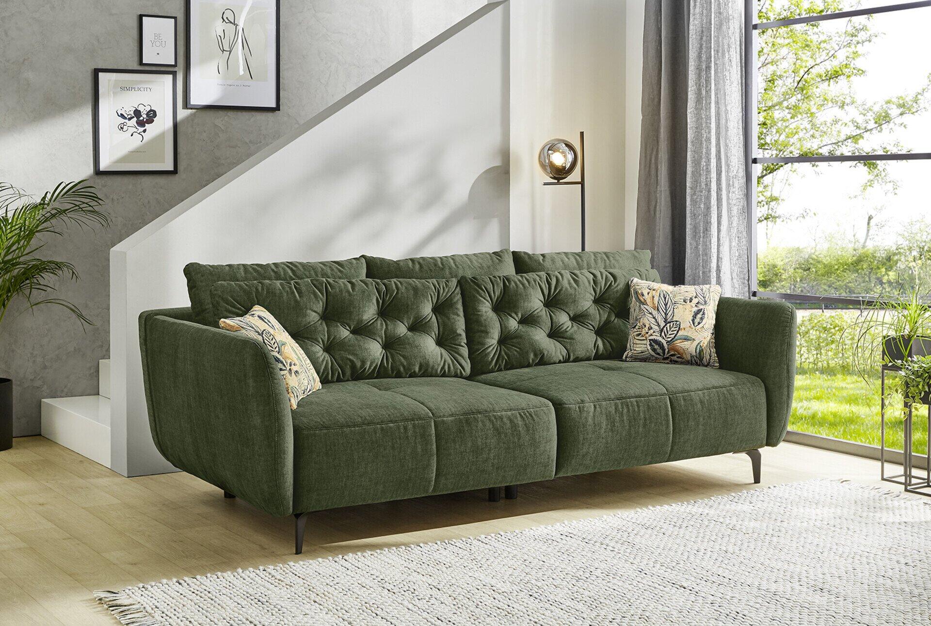 Dunkelgrüne Eckcouch Big Sofa, Spa, mit hoher Rückenlehne und breiten Armlehnen, auf schlanken Füßen, in einem hellen Wohnzimmer.