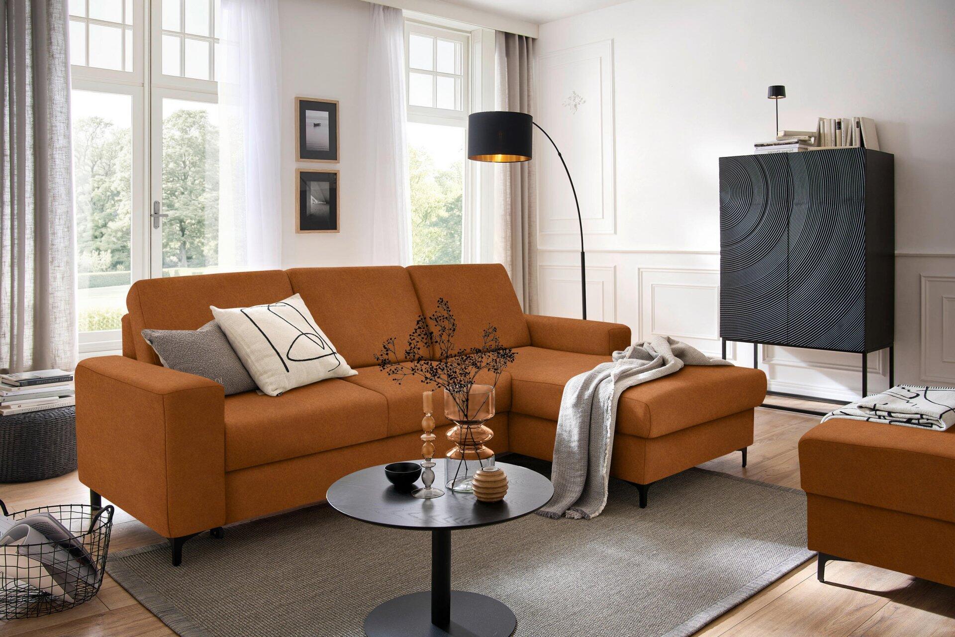 Ecksofa Balina in L-Form mit Winkelfüßen, Bettkasten und Schlaffunktion, abgebildet aus der Seitenperspektive in einem hellen Wohnzimmer.