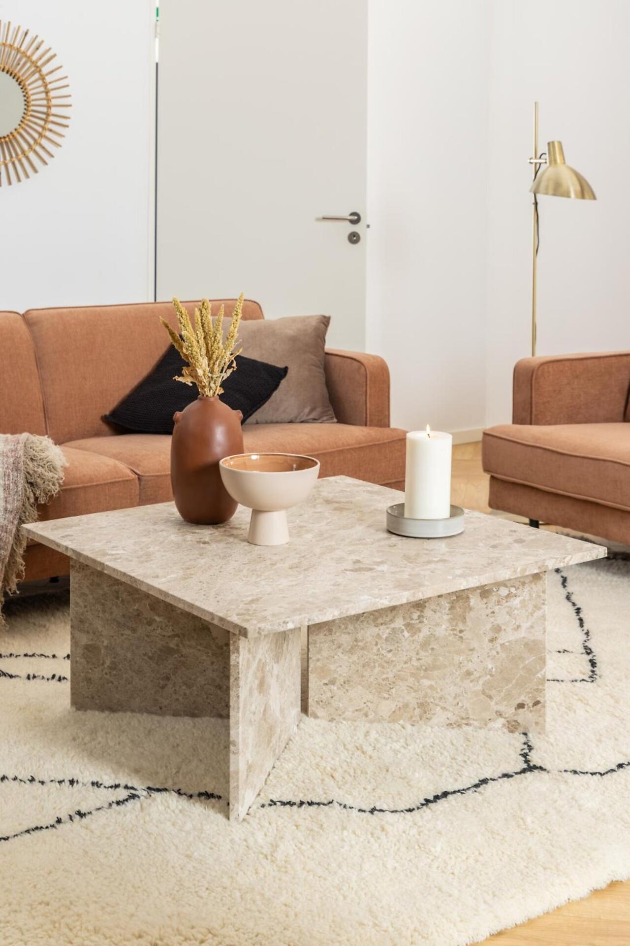Couchtisch Vega mit minimalistischem Marmordesign und leicht erhöhter Kante, präsentiert auf einer erhöhten Perspektive mit dekorativen Elementen.