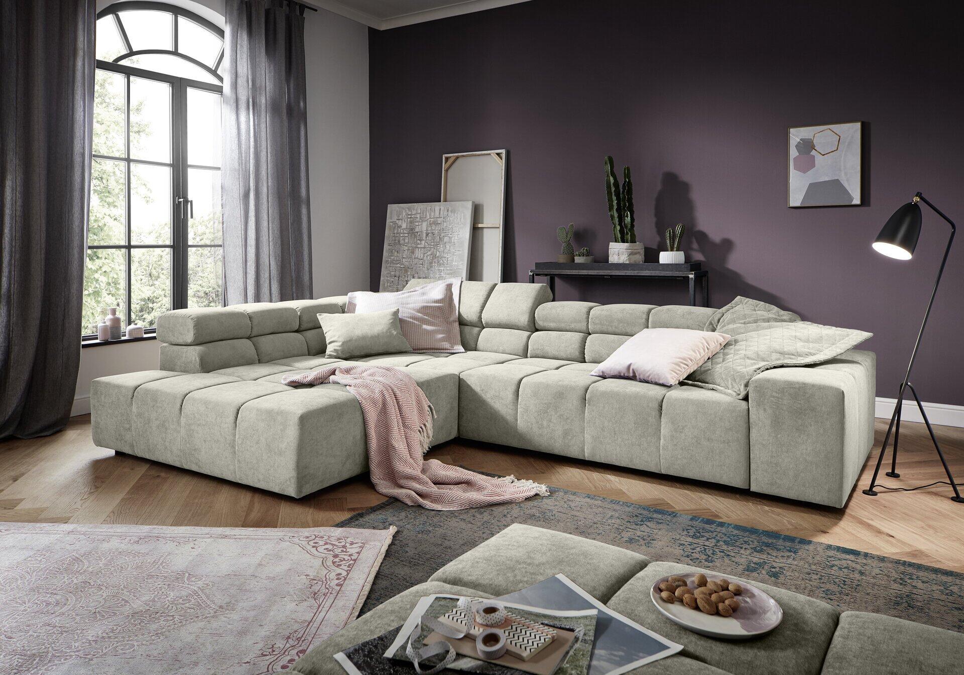 Modulares Ecksofa Omega 2.0 in hellgrau mit Kopfteilverstellung und Eckausbildung, leicht erhöht fotografiert mit Dekorationsgegenständen auf der Sitzfläche.
