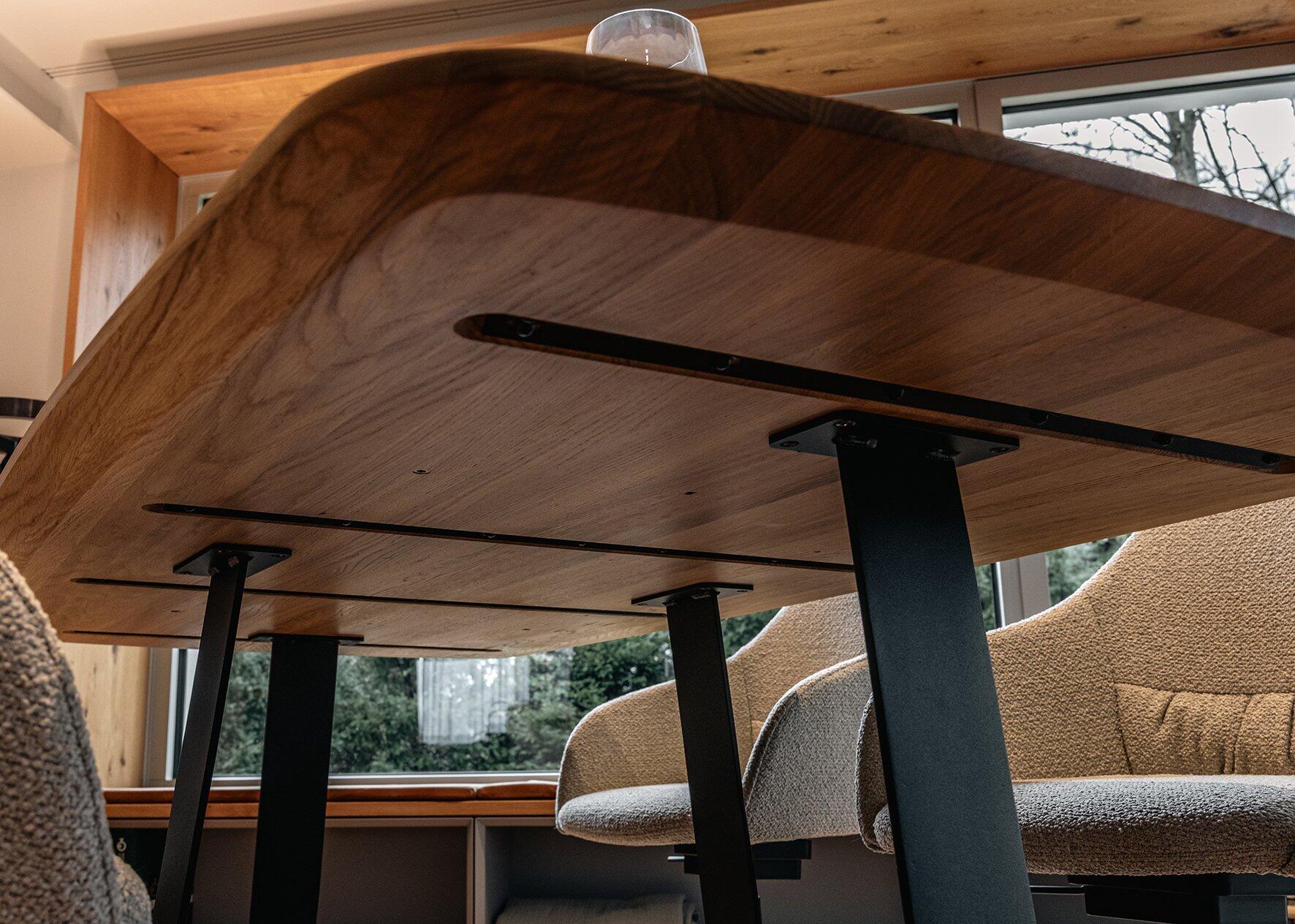 Esszimmertisch Urban mit Eichentischplatte und bootsförmigem Design, gezeigt aus einer unteren Perspektive, die die organische Kante und die schwarzen Metallbeine betont.