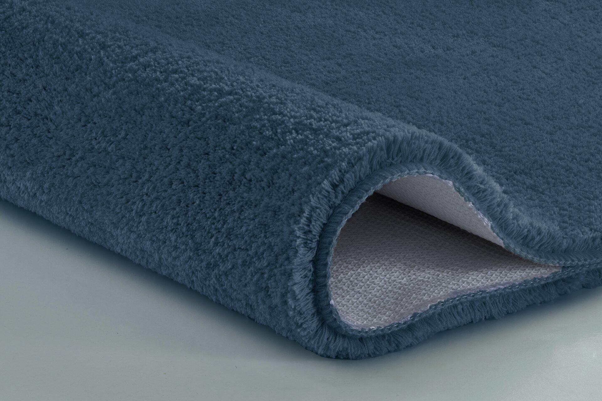 Badteppich Marco, stahlblau, flauschig und zur Hälfte aufgerollt, um Unterseite mit strukturierter Oberfläche zu zeigen.