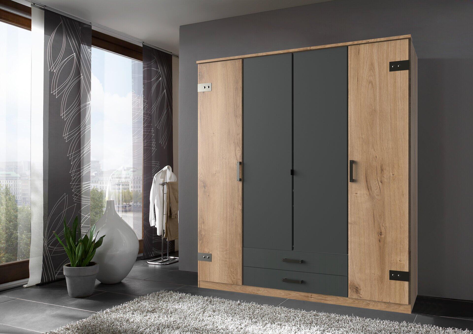 Kleiderschrank Cork in Graphit mit drei Türen, zwei Schubladen und sichtbaren Einlegeböden, dargestellt in einer Innenraumansicht mit frontalem Blick auf die Holzoptik der oberen Türen und die graue untere Tür.