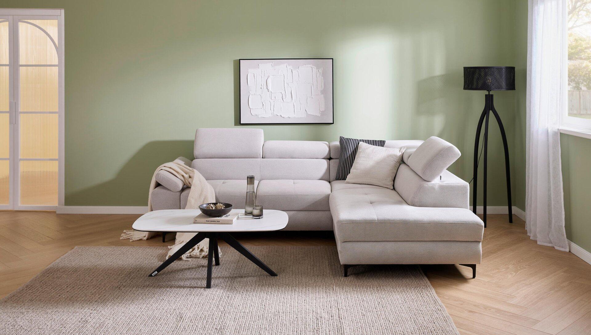 Ecksofa Combo in hellgrau/beige mit abklappbarer Kopfstütze, verstellbaren Arm- und Kopfteilen sowie Ottomane, aus einer seitlichen Perspektive im stilvoll eingerichteten Wohnzimmer.