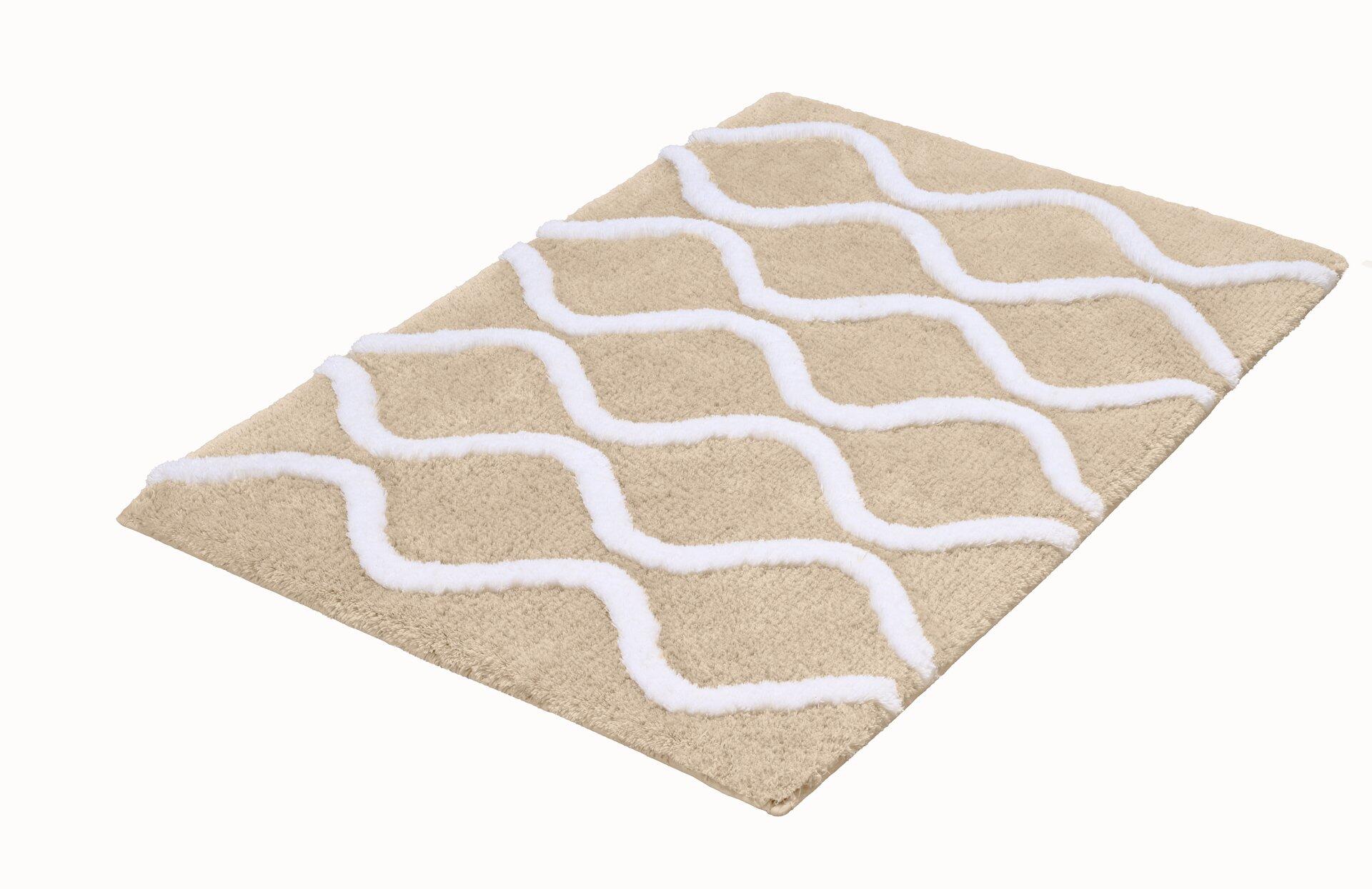 Sandbeige Badteppich Piana mit weißem, wellenförmigem Muster und flauschiger Textur, aus der Vogelperspektive sichtbar.