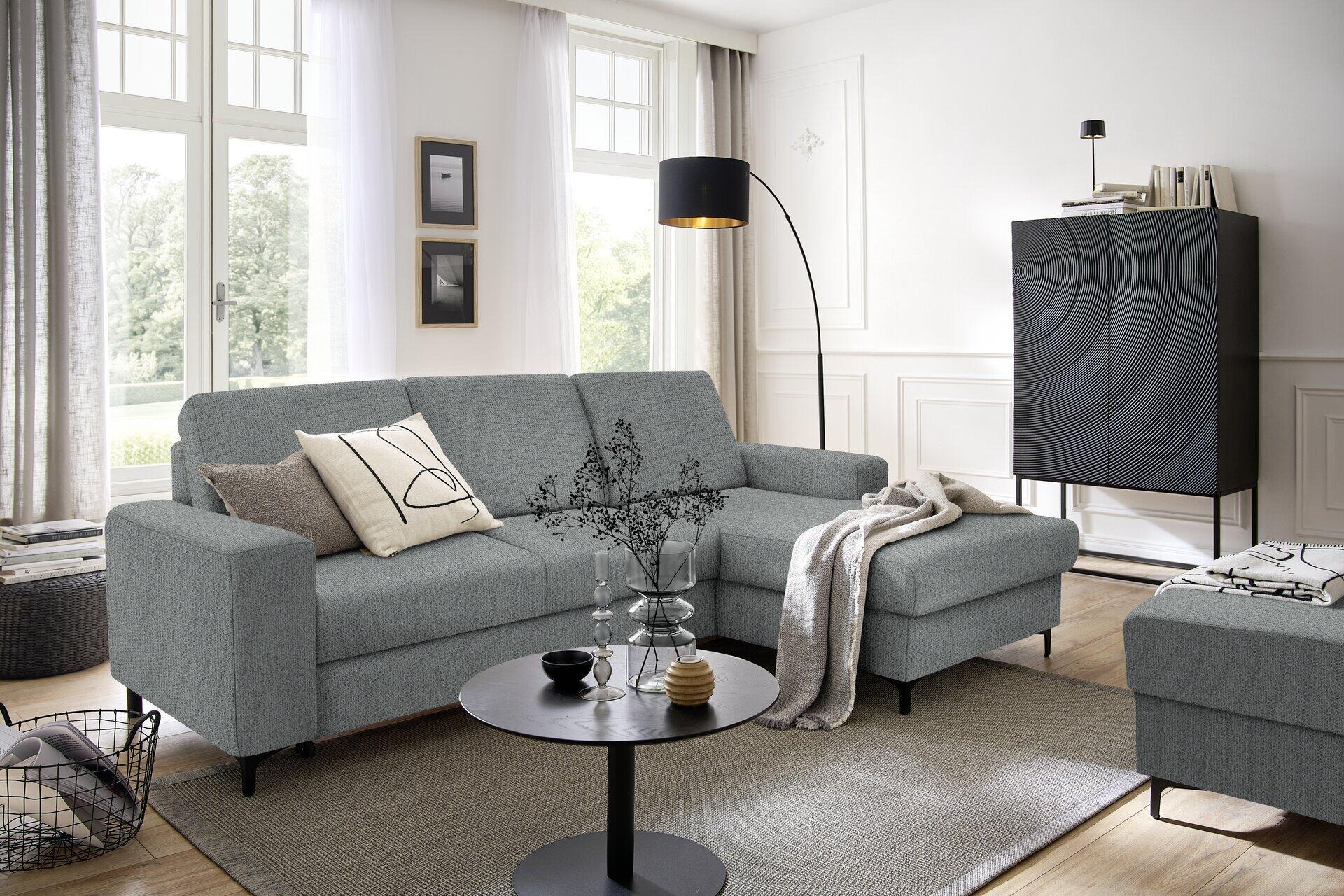 Ecksofa Balina mit rechts liegender Ottomane, Winkelfüßen in Schwarz und integriertem Bettkasten, aus einer leicht erhöhten Perspektive fotografiert, um die L-Form und die Anordnung im Wohnzimmer zu zeigen.
