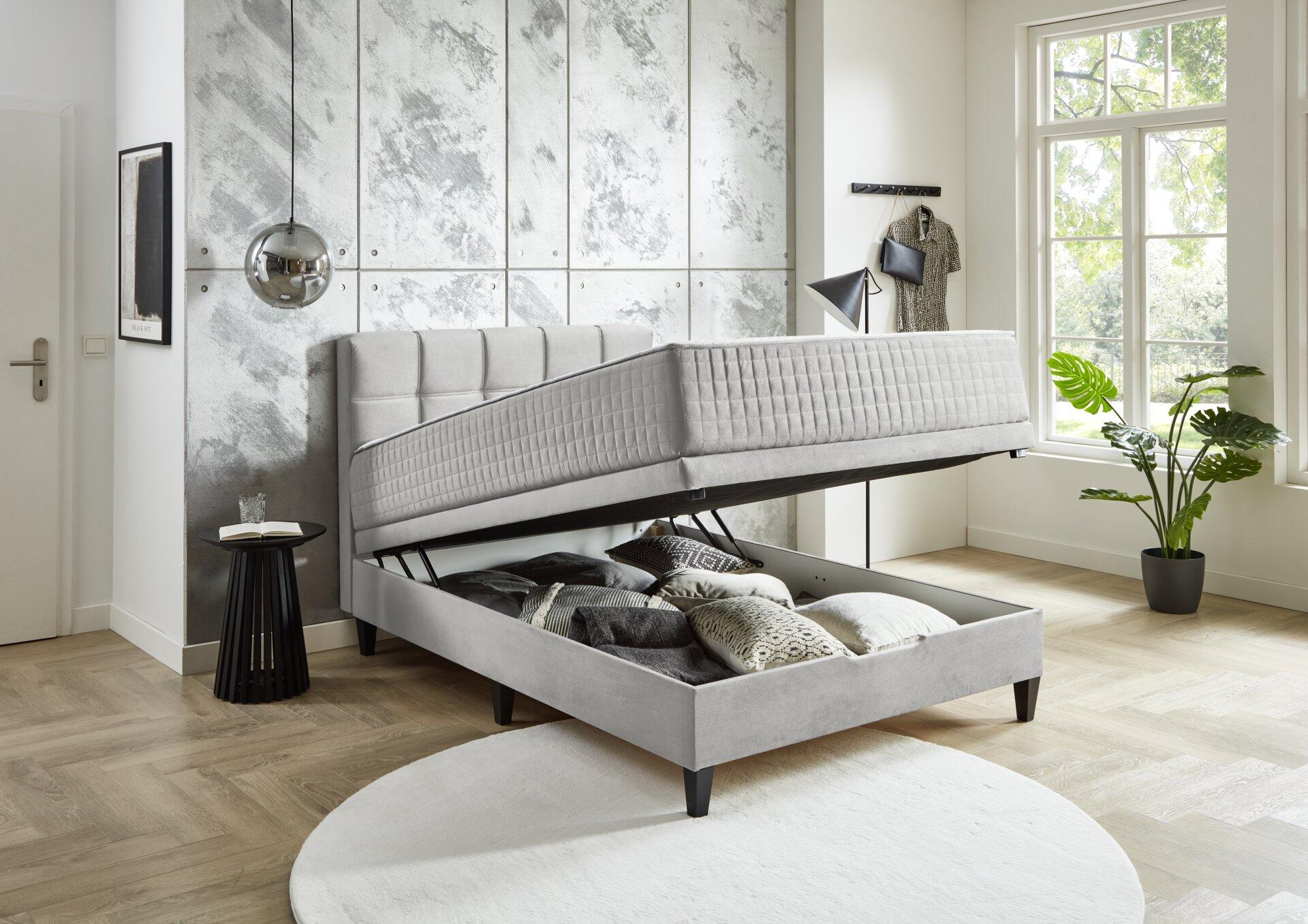 Boxspringbett Wien BX2590 mit grauem Stoffbezug und gestreiftem Kopfteil, zeigt den integrierten Bettkasten mit Stauraum für Kissen und Decken.