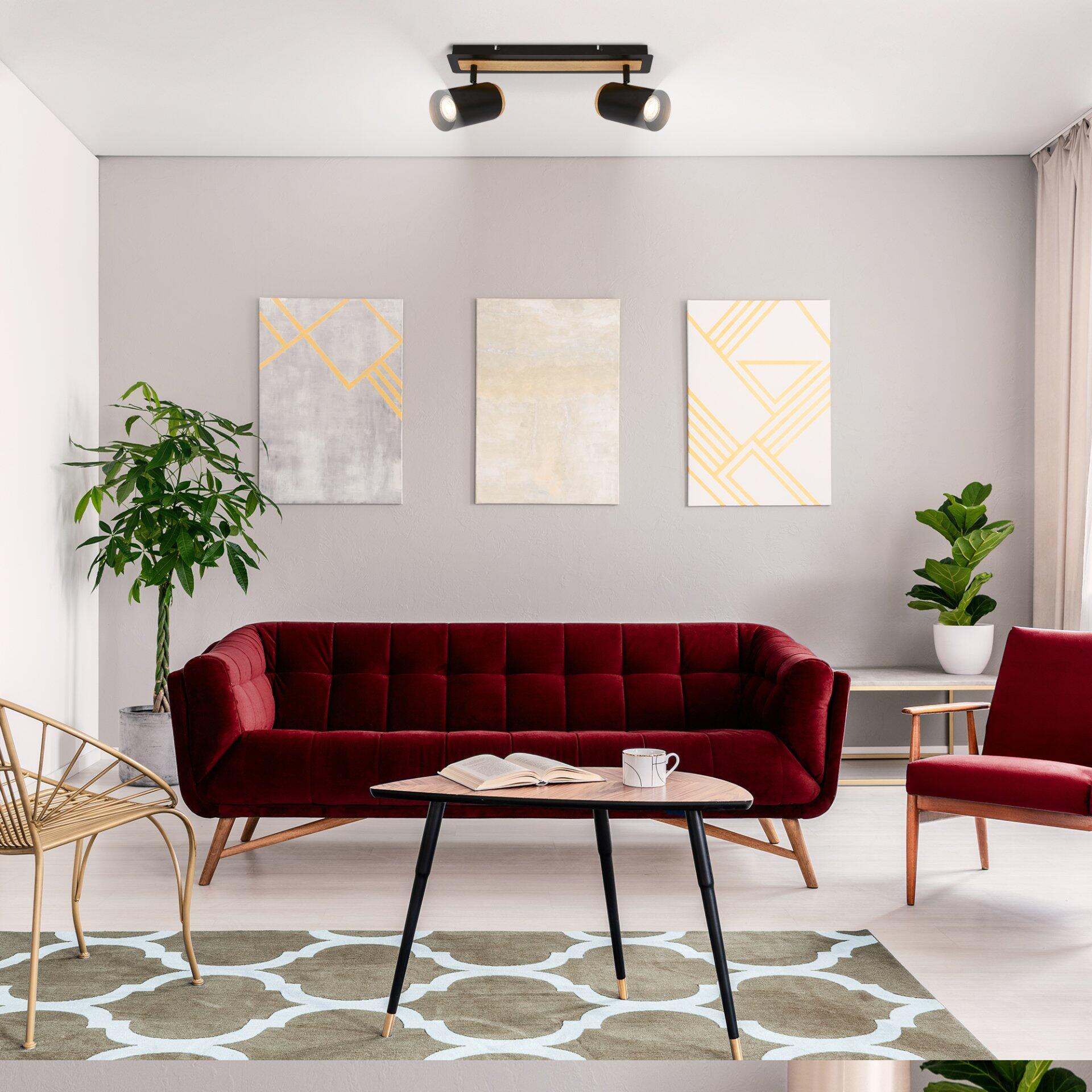 Elegantes, tiefrotes Samtsofa Spot, Duta, mit abgerundeten Ecken, geschwungener Rückenlehne und goldenen Füßen, präsentiert in einem stilvoll eingerichteten Wohnzimmer mit passenden Sesseln und Couchtisch.