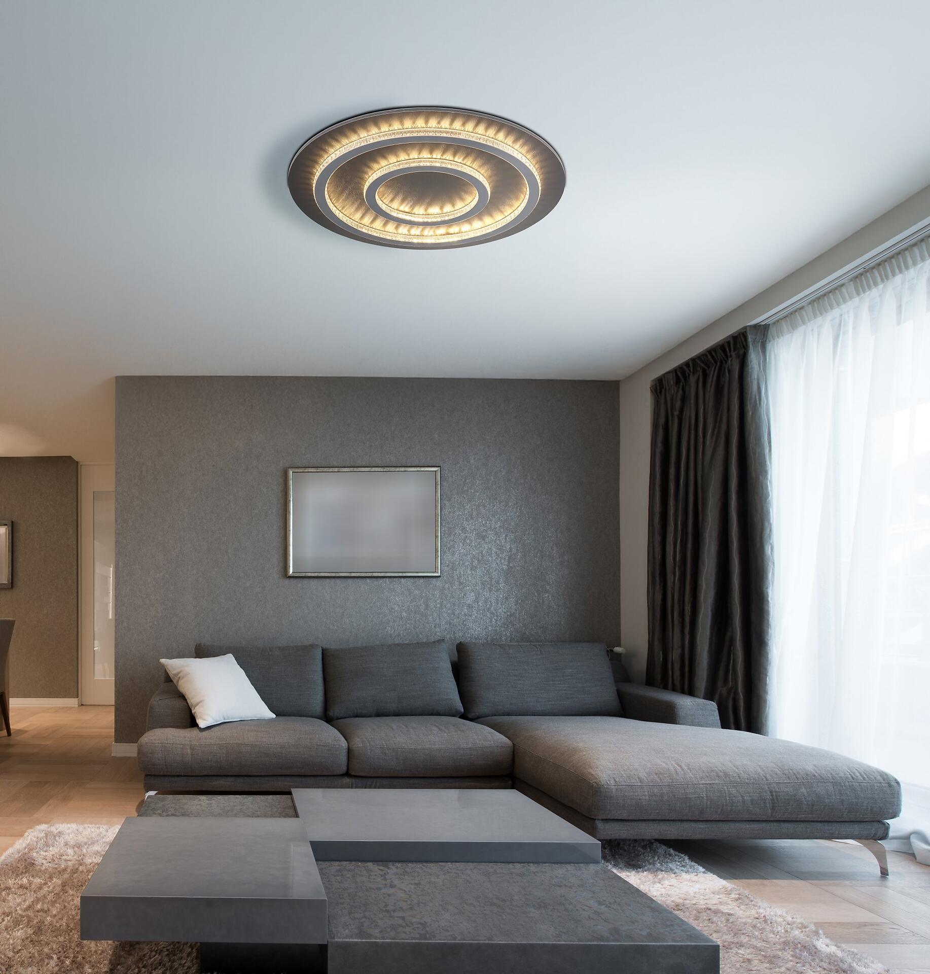 Deckenleuchte JAYDEN mit mehrschichtigem Kunststoffkristall-Design und indirekter Beleuchtung, integriert in ein modernes Wohnzimmer.