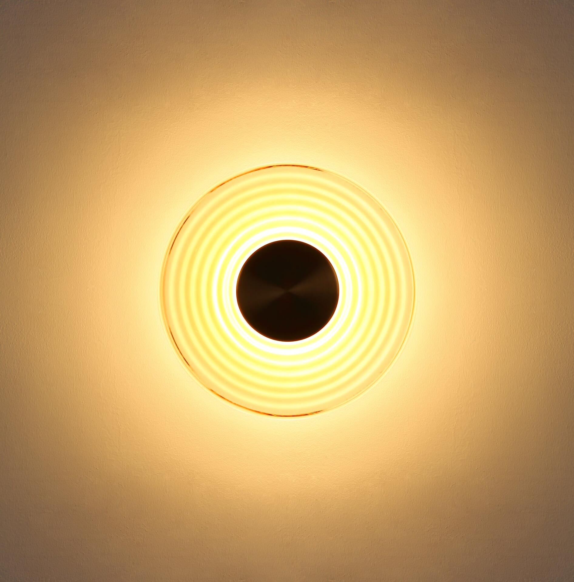Wandleuchte JANELL mit konzentrischen Lichtringen, dargestellt in frontaler Perspektive an einer hellen Wand.