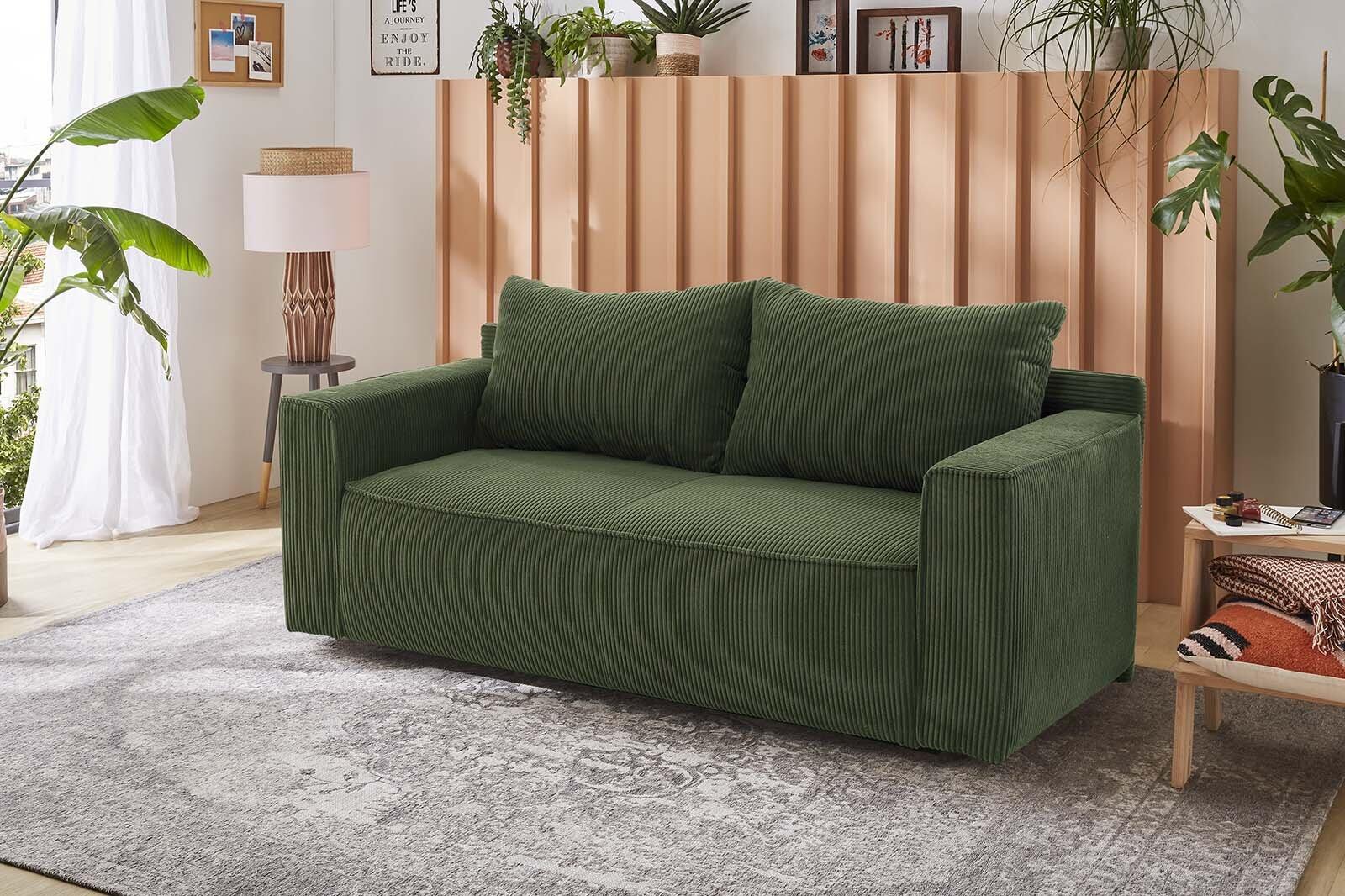 Grünes Schlafsofa Ron mit breiten Armlehnen und hoher Rückenlehne, präsentiert in einer Innenraumumgebung mit Holzpaneelen und Zierkissen.