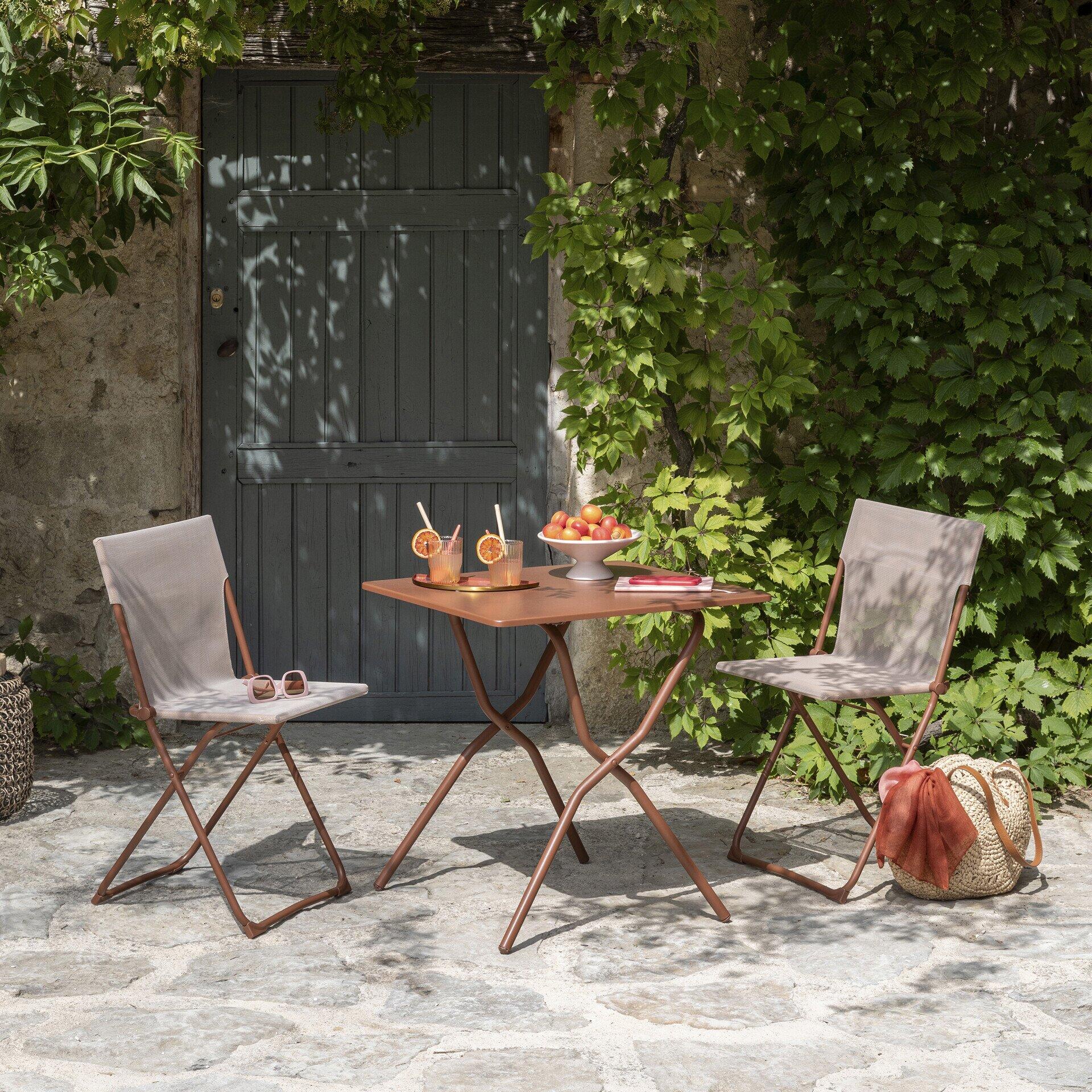 Runder Gartentisch Balcony Canyon Tube Canyon mit faltbaren Gartenstühlen und Accessoires auf gepflastertem Hof, ideal für gemütliche Outdoor-Momente.