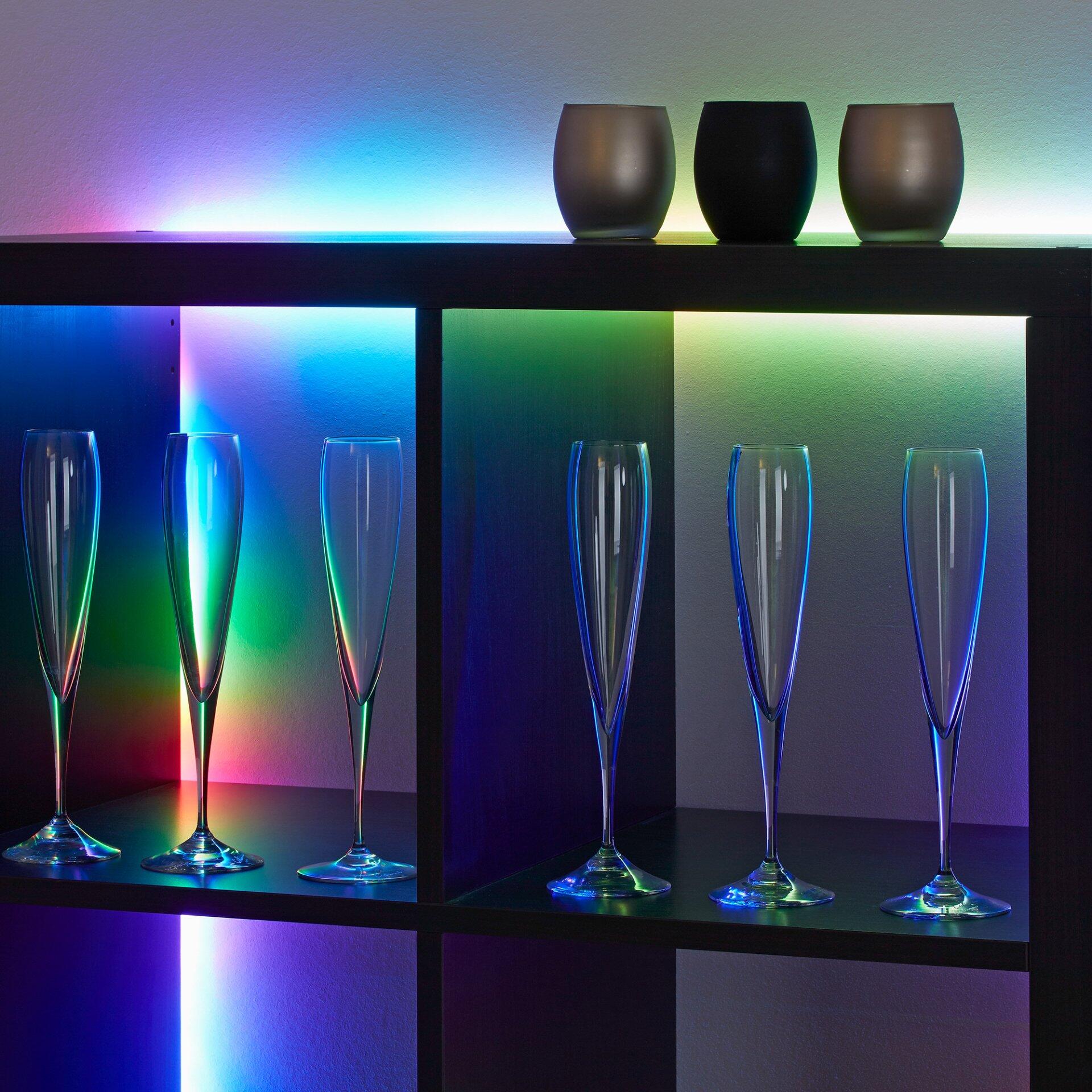 LED Band BRILO beleuchtet eine moderne Regalkonstruktion in verschiedenen Farben, wobei das Licht von oben und den Seiten auf Champagnergläser und dekorative Kerzenständer fällt.