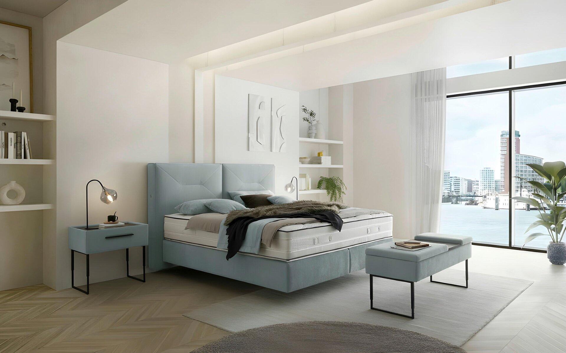 Luxor Line Boxspringbett mit hellblau/grauem Kopfteil und gefüllter Optik, fotografiert aus leicht erhöhter Vogelperspektive in einem hellen Schlafzimmer.
