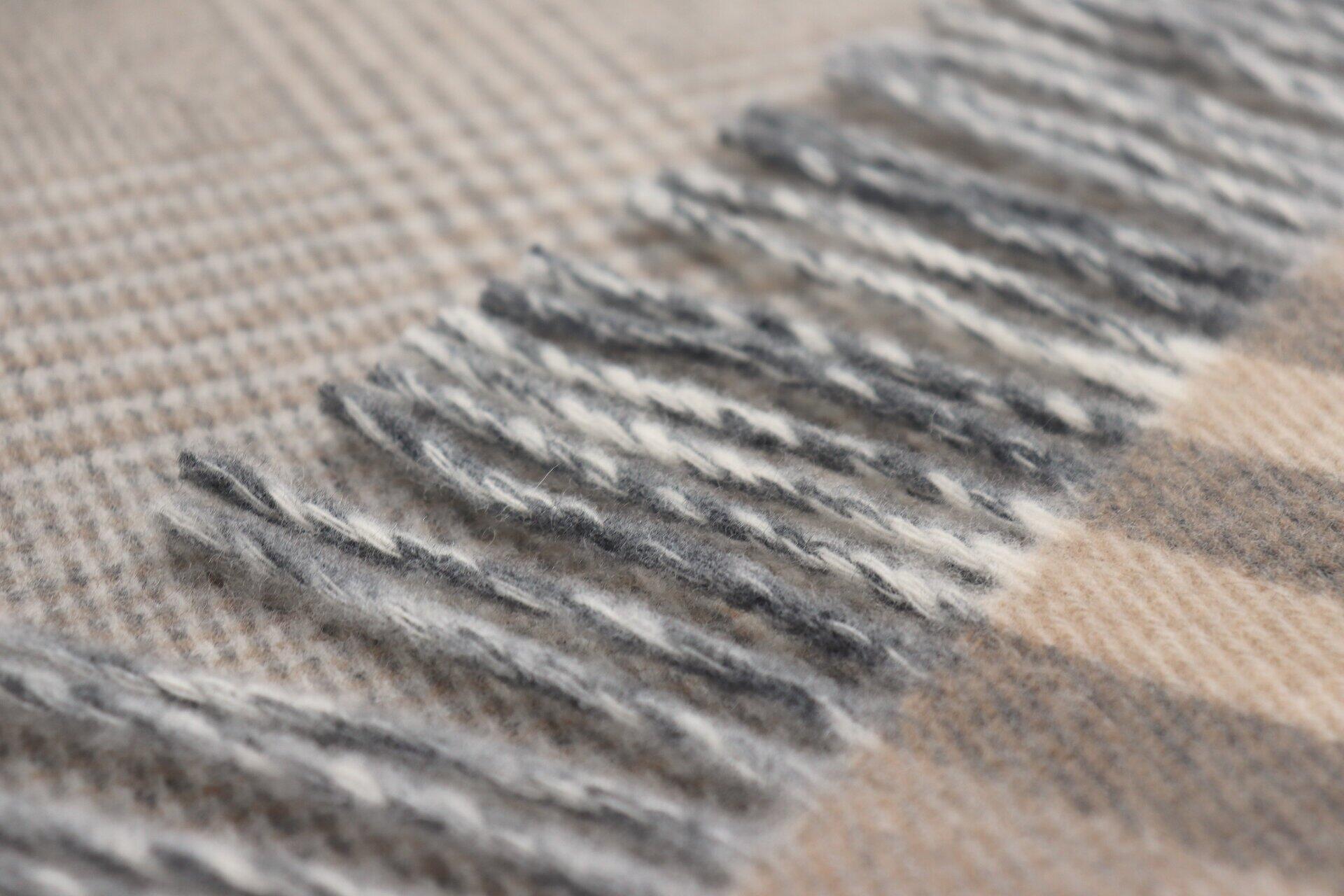 Nahaufnahme eines karierten Plaid aus Wolle und Kaschmir mit fransigen Rändern in Beige- und Grau-Tönen.