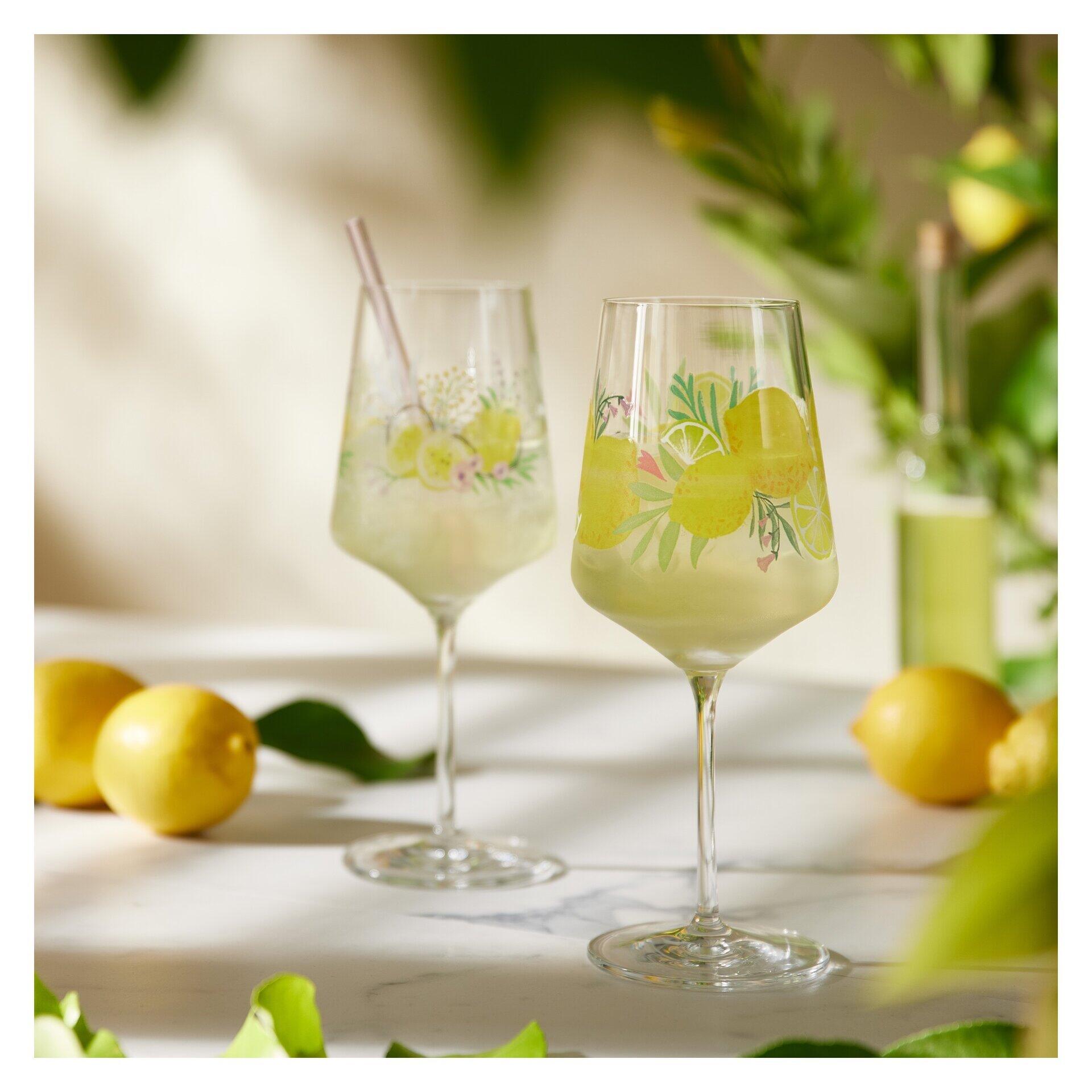 Zwei dekorierte Aperitifgläser mit Zitronen-Blumen-Motiv und einem goldenen Trinkhalm, präsentiert auf marmoriertem Untergrund in einer leicht erhöhten Perspektive.
