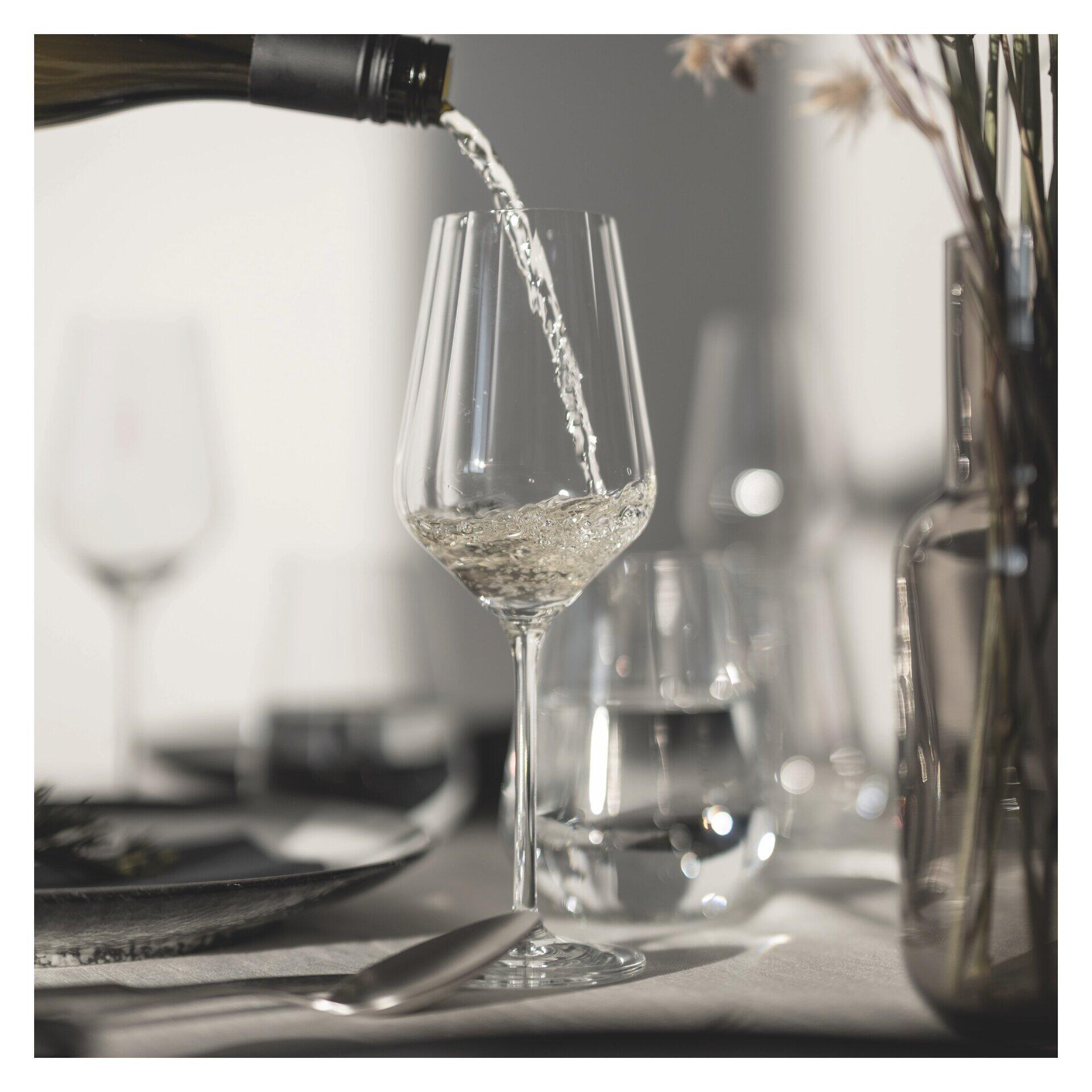 Weißwein- und Wasserglas-Set mit reliefierter Struktur, Detailaufnahme beim Eingießen von Wein in einen schlanken Kelch mit langem Stiel.