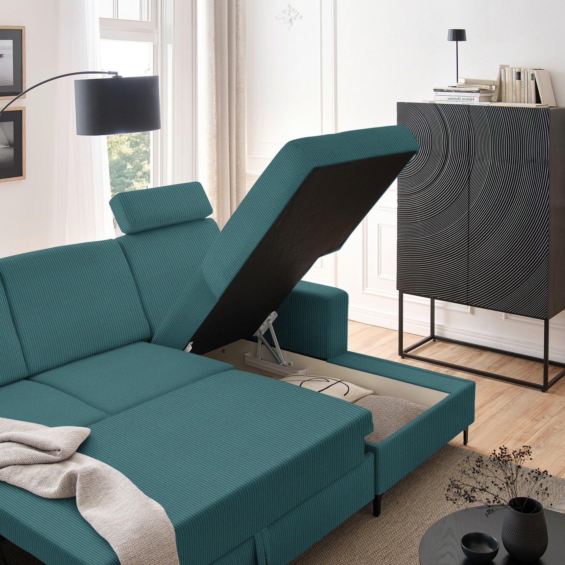 Türkisfarbenes Ecksofa Balina mit geöffneter Rückenlehne und Bettdecke auf der Liegefläche, das durch ein Gasdrucksystem flachgestellt wird, in einer Innenraumansicht.