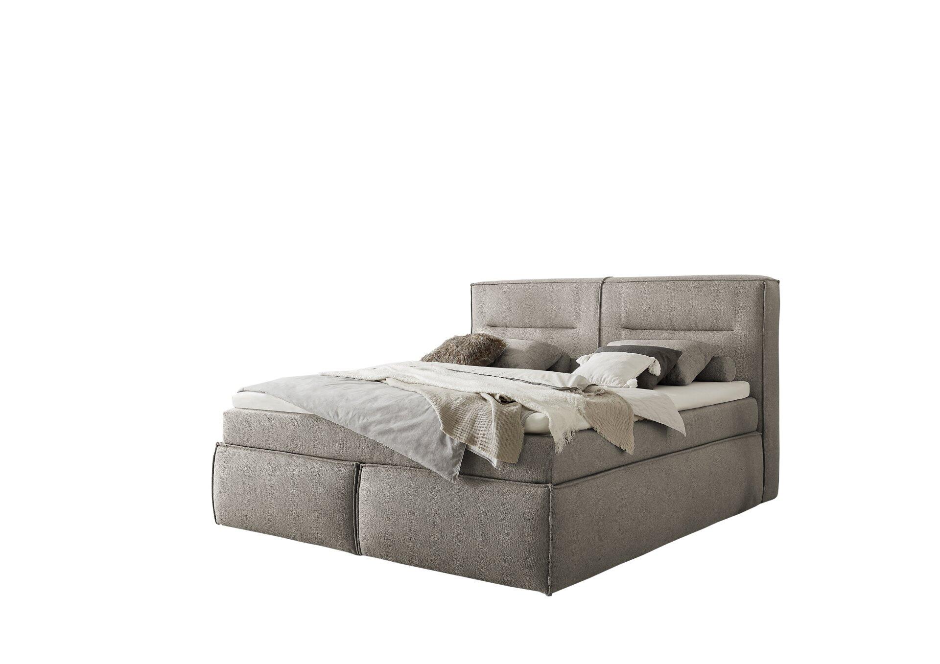 Boxspringbett Las Vegas mit grauem Stoffbezug, hohem Kopfteil und Duo-Matratze, dargestellt in einem hellen Schlafzimmer mit zwei Personen beim Lesen.