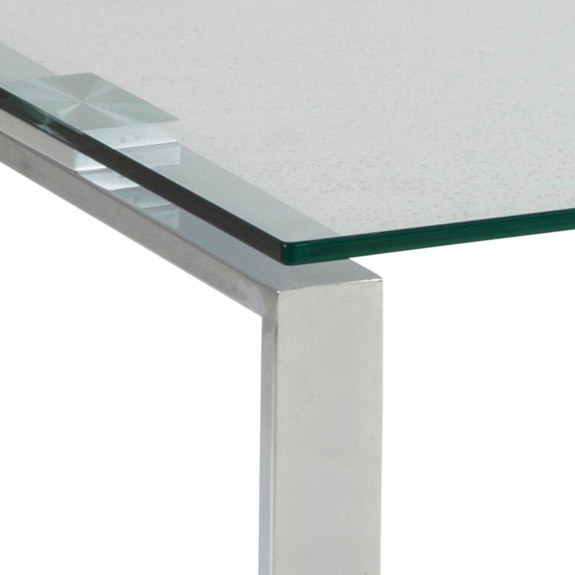 Quadratischer Couchtisch Katrine mit transparentem, bläulich schimmerndem Glas und glänzendem silbernen Metallgestell, aufgenommen aus einer leicht seitlichen, unteren Perspektive.