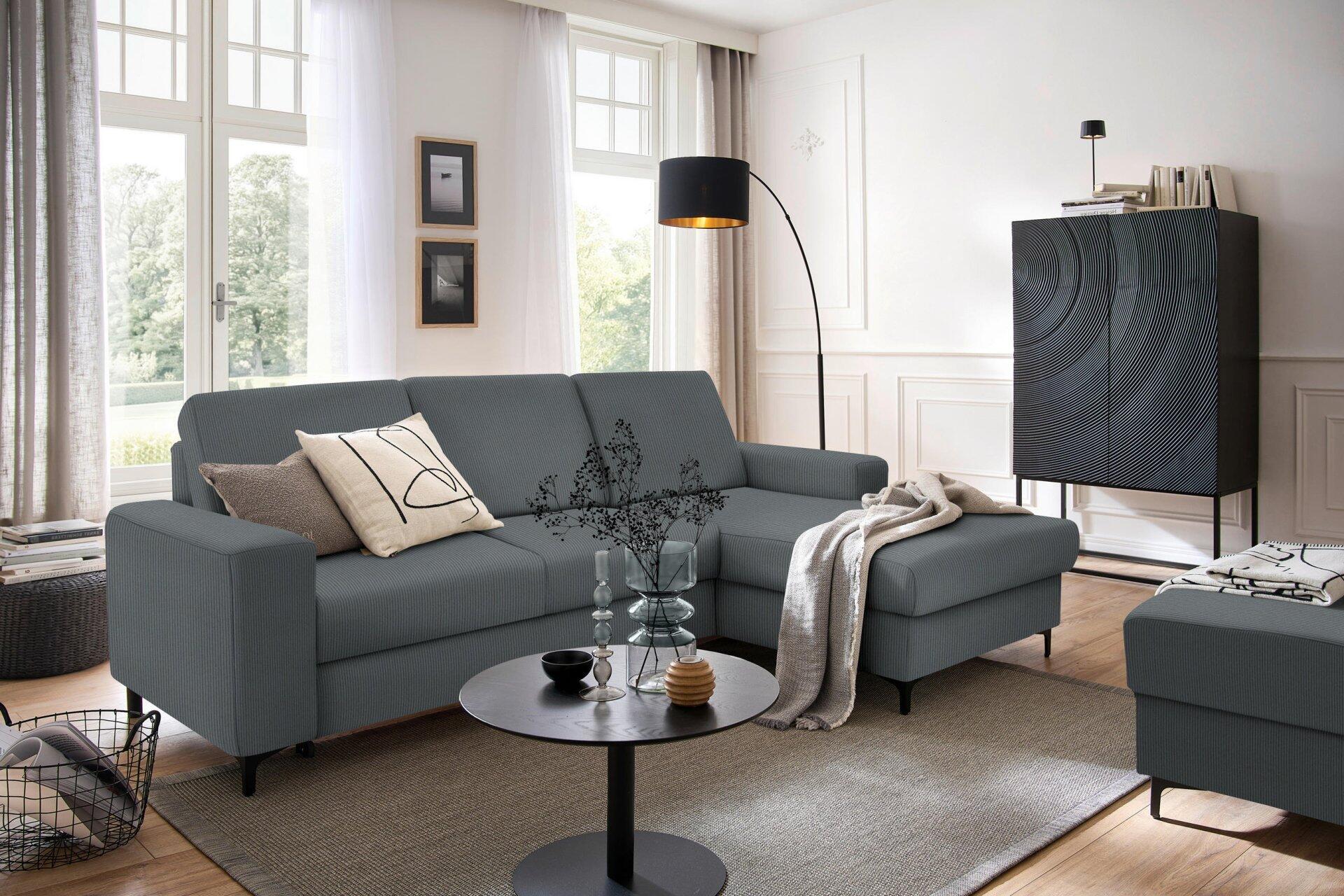 Graues Ecksofa Balina mit Winkelfüßen, rechtsseitigem Fußteil und ausgezogener Schlaffunktion in einem modernen Wohnzimmer.