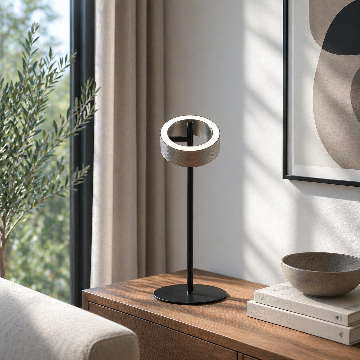 Tischleuchte Axion mit schwenkbarem Lampenkopf und Touchdimmer, dargestellt auf einer Holztruhe in einer eleganten, von unten aufgenommenen Perspektive.