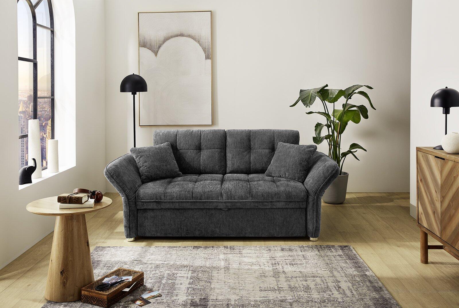 Schlafsofa Leon in grau mit gepolsterten Rechteck-Rückenlehnen und zwei Rückenkissen, frontal dargestellt im minimalistischen Wohnzimmer.