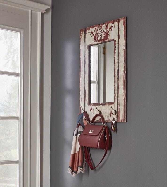 Wandgarderobe mit rustikalem Holzrahmen, drei Haken für Accessoires und eingelassenem Spiegel, dargestellt aus schräger Perspektive an einer grauen Wand.