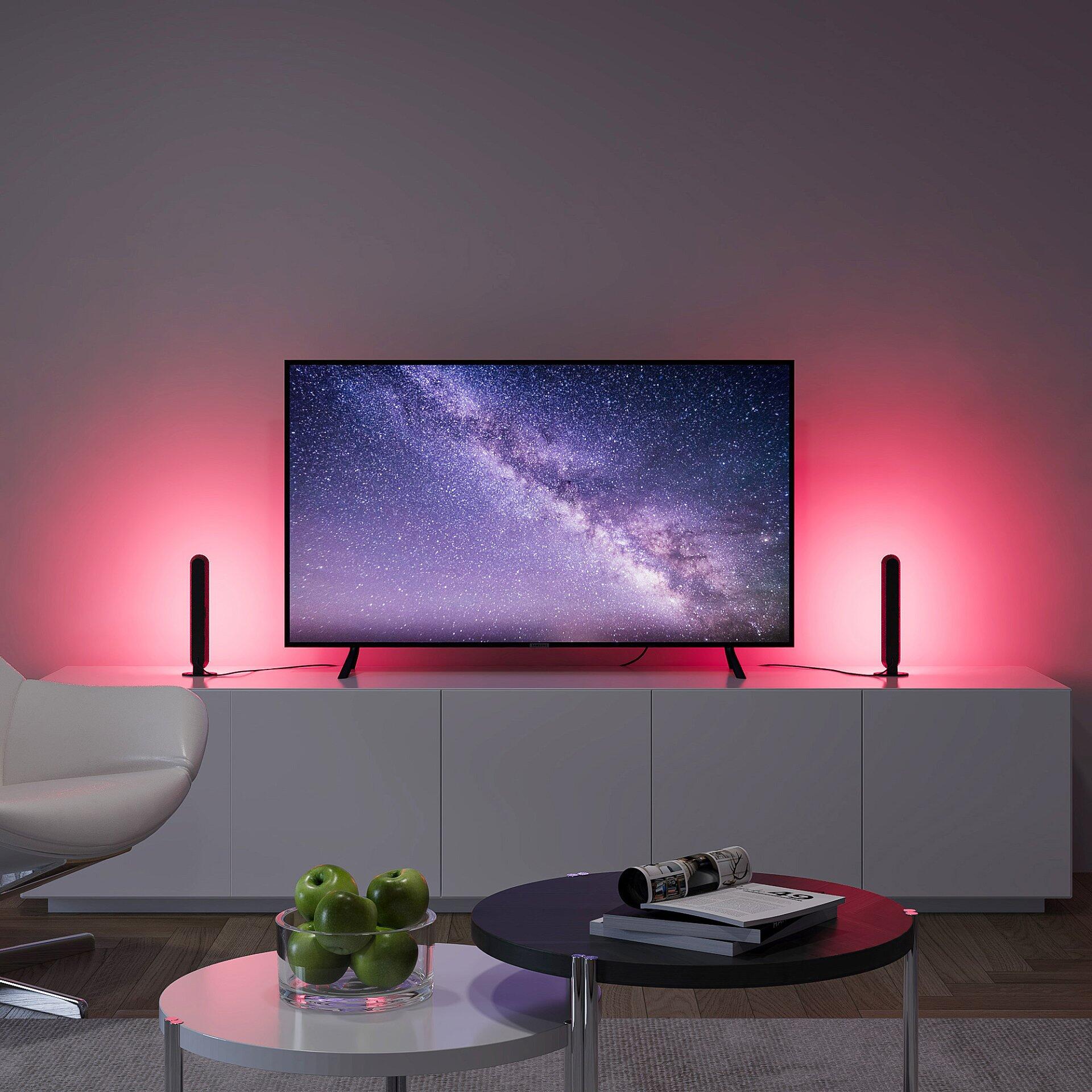 Vertikale LED-Leuchten beleuchten in einem Wohnzimmerambiente einen flachen Fernseher und eine grifflose TV-Bank, ergänzt durch eine Tischleuchte Game.