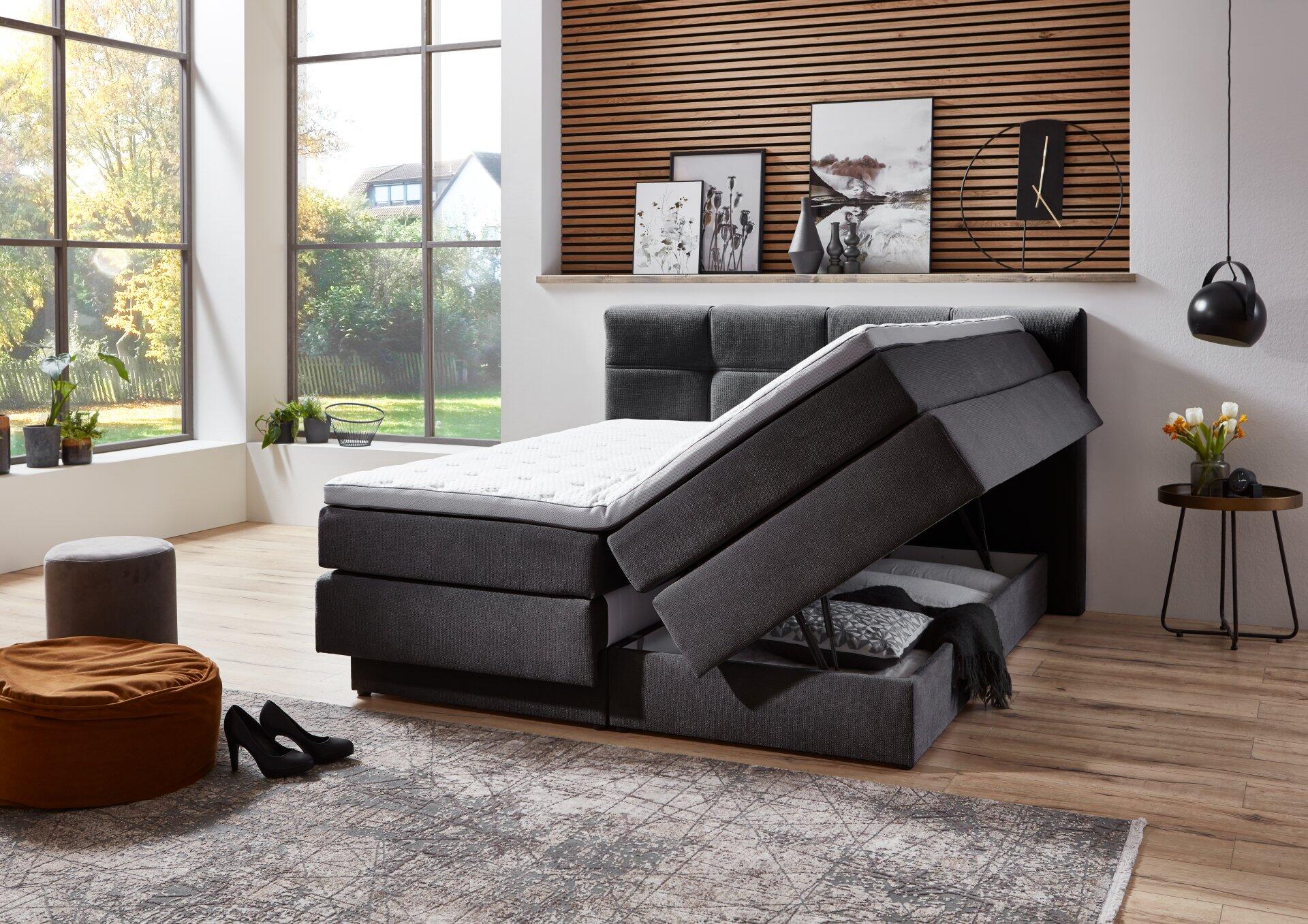 Boxspringbett Portage BX2110 mit grau gestepptem Kopfteil und integriertem Bettkasten, der erhöhten Stauraum für Bettwäsche zeigt.