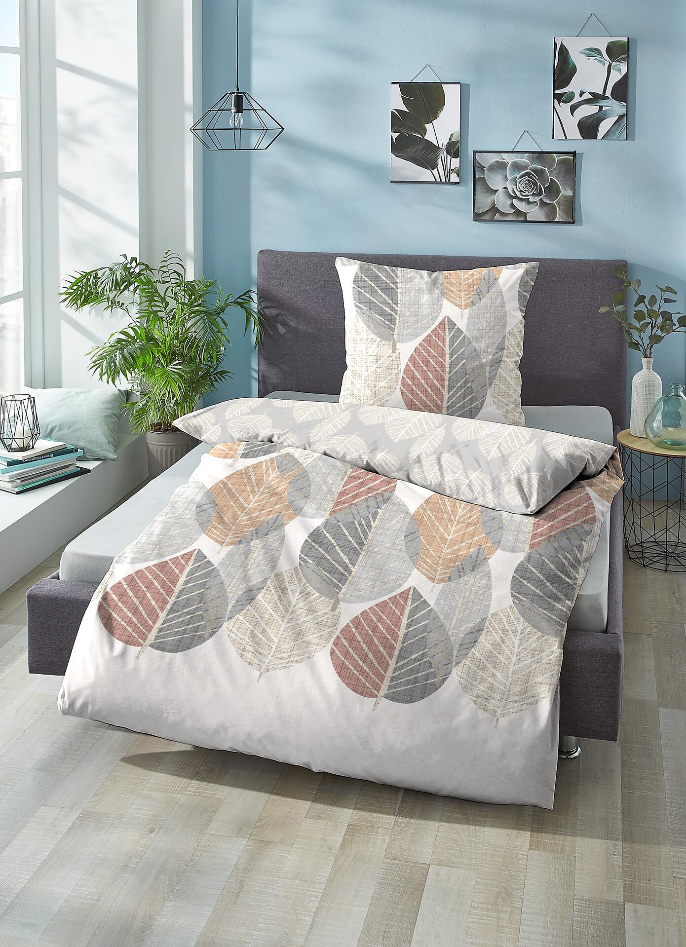 Biberna Bettbezug mit stilisiertem Blättermotiv in Grau-, Beige- und Rostrot-Tönen auf einem Bett in einem hellen Schlafzimmer.
