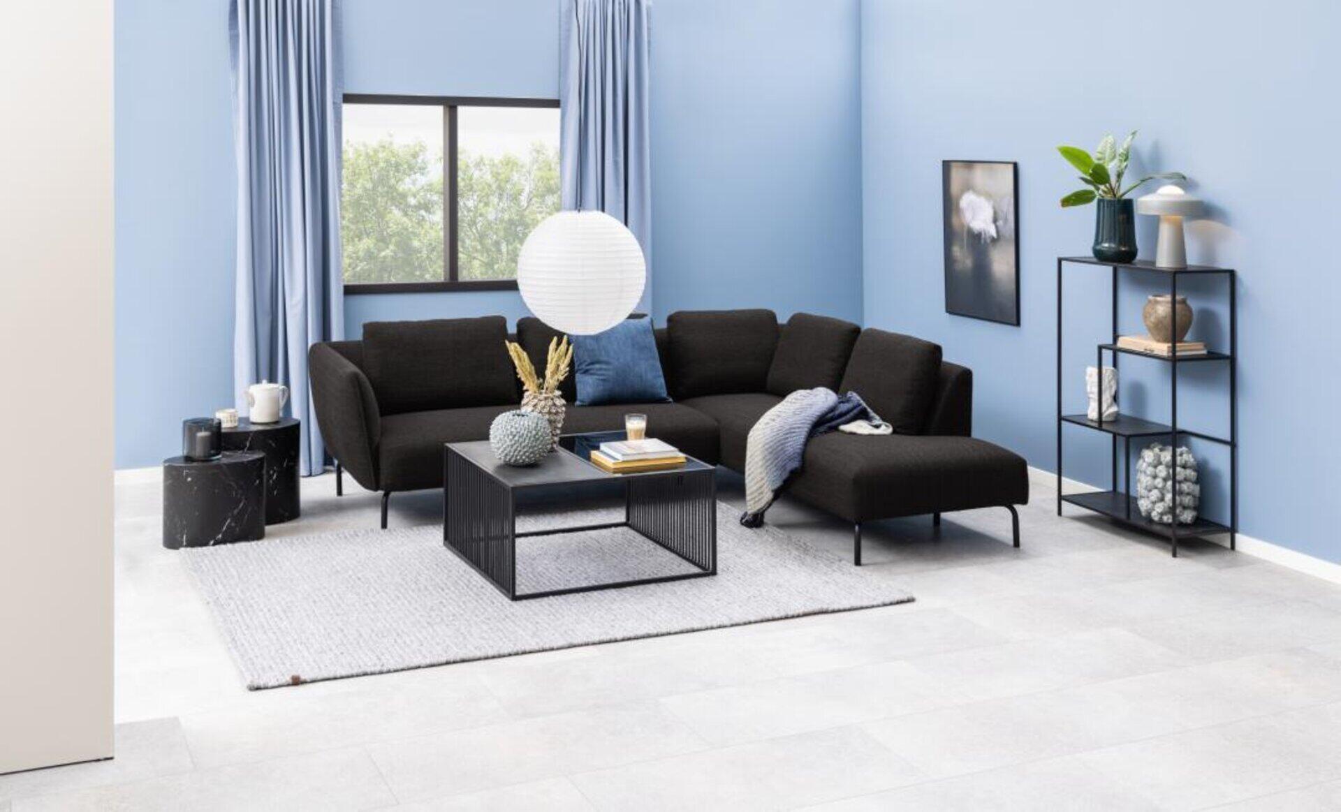 Couchtisch Strington mit schwarzem Metallgestell und Glasplatte vor einer grauen Eckcouch in einem stilvollen Wohnzimmer.