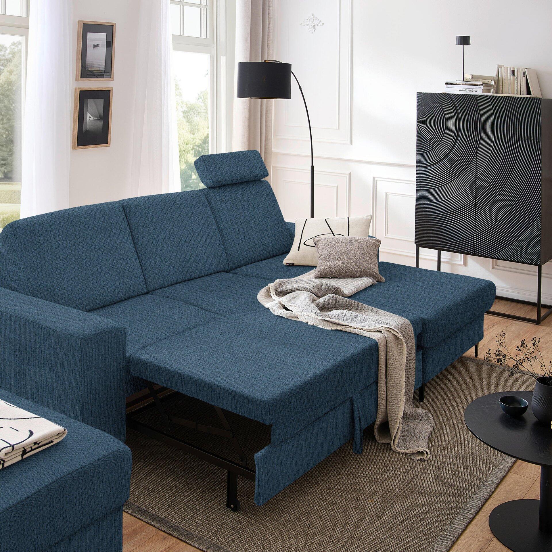 Blaues Ecksofa Balina mit Schlaffunktion und ausgezogenem Liegeelement, Blickwinkel von der Seite und leicht erhöht, zeigt das Sofa in seiner Gesamtheit mit angrenzender Einrichtung.