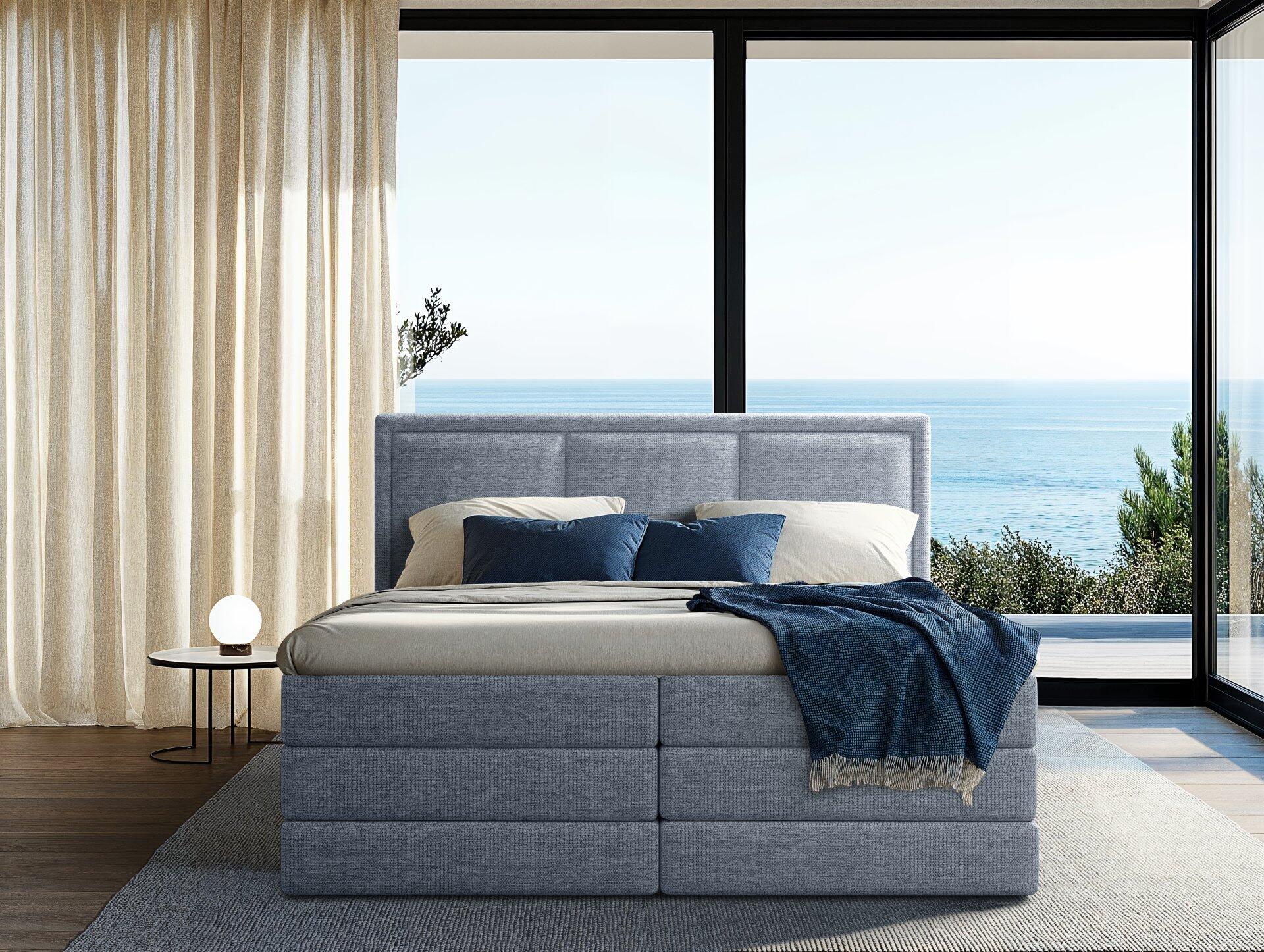 Boxspringbett Swing mit grauem Stoffbezug, hohem, gesteppten Kopfteil und mehreren dekorativen Kissen.