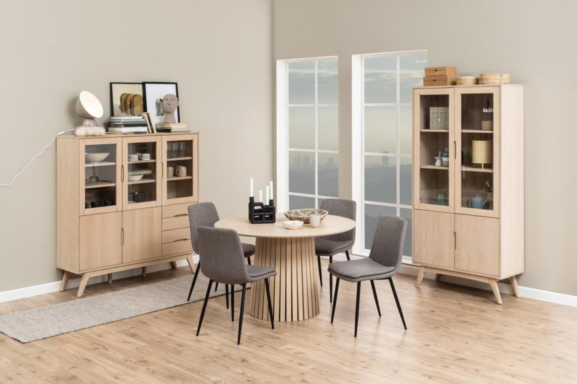 Esszimmerstuhl Becca mit grauem Bezug und schwarzem Metallgestell, präsentiert in einem modernen Essbereich mit rundem Tisch und Teppich.