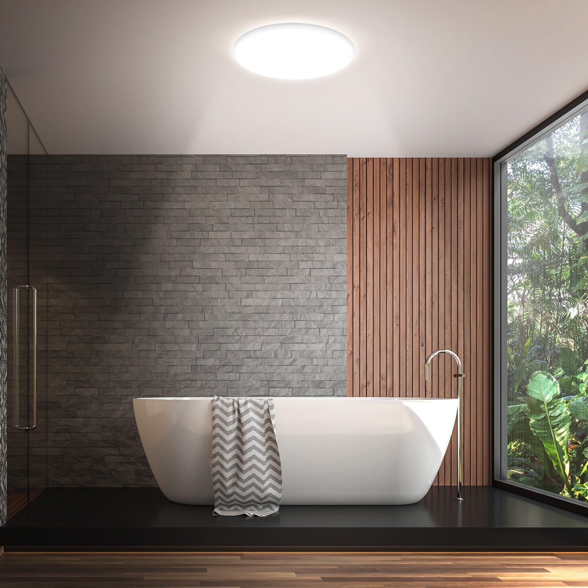 Weiße Wand- und Deckenleuchte Rowny über einer Badewanne in einem modernen Badezimmer mit Blick auf Grünflächen.