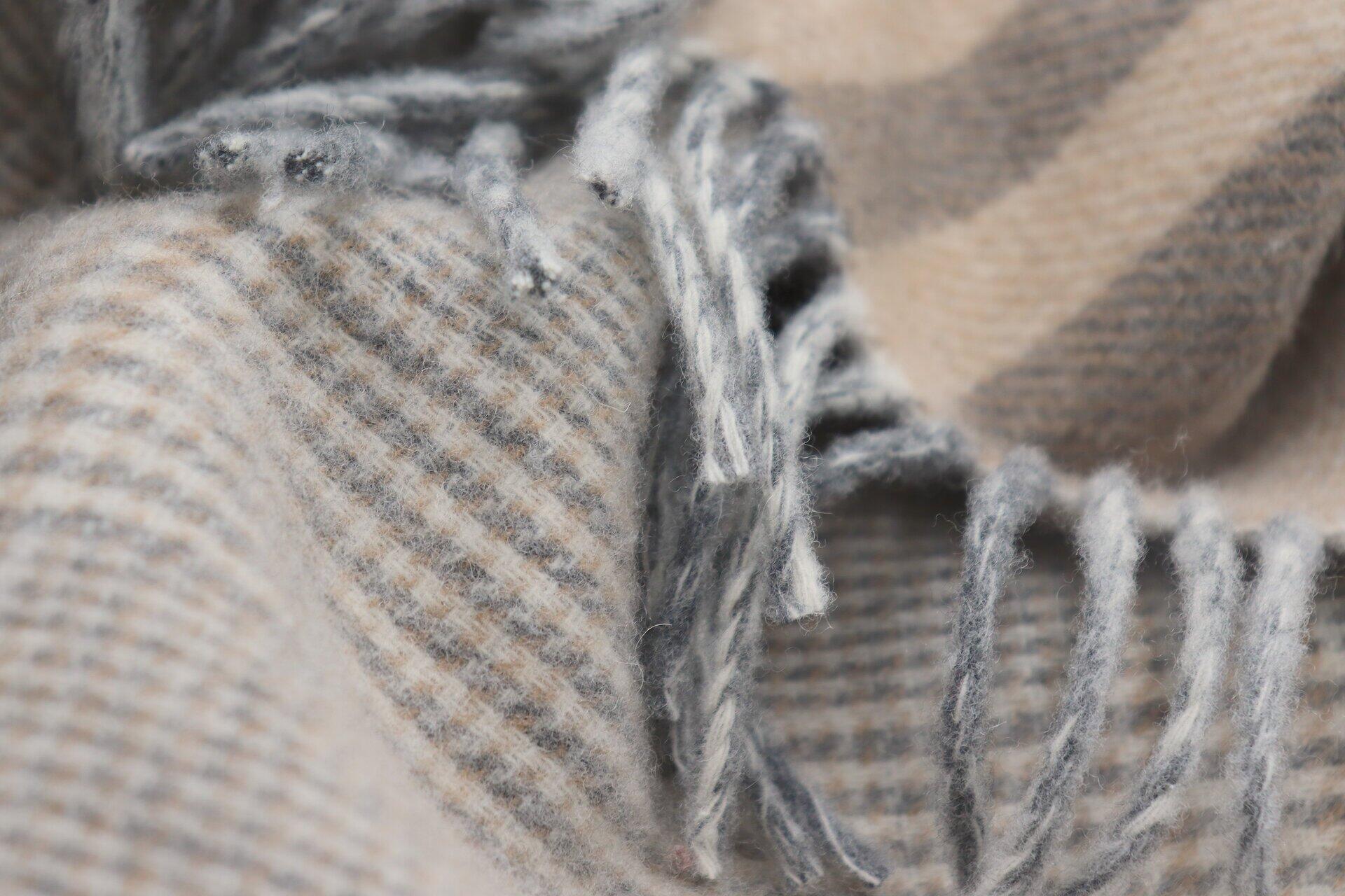 Nahaufnahme eines grob gewebten Plaid Teppichs mit Karo-Muster in Beige, Grau und Weiß und ausgefransten Kanten.