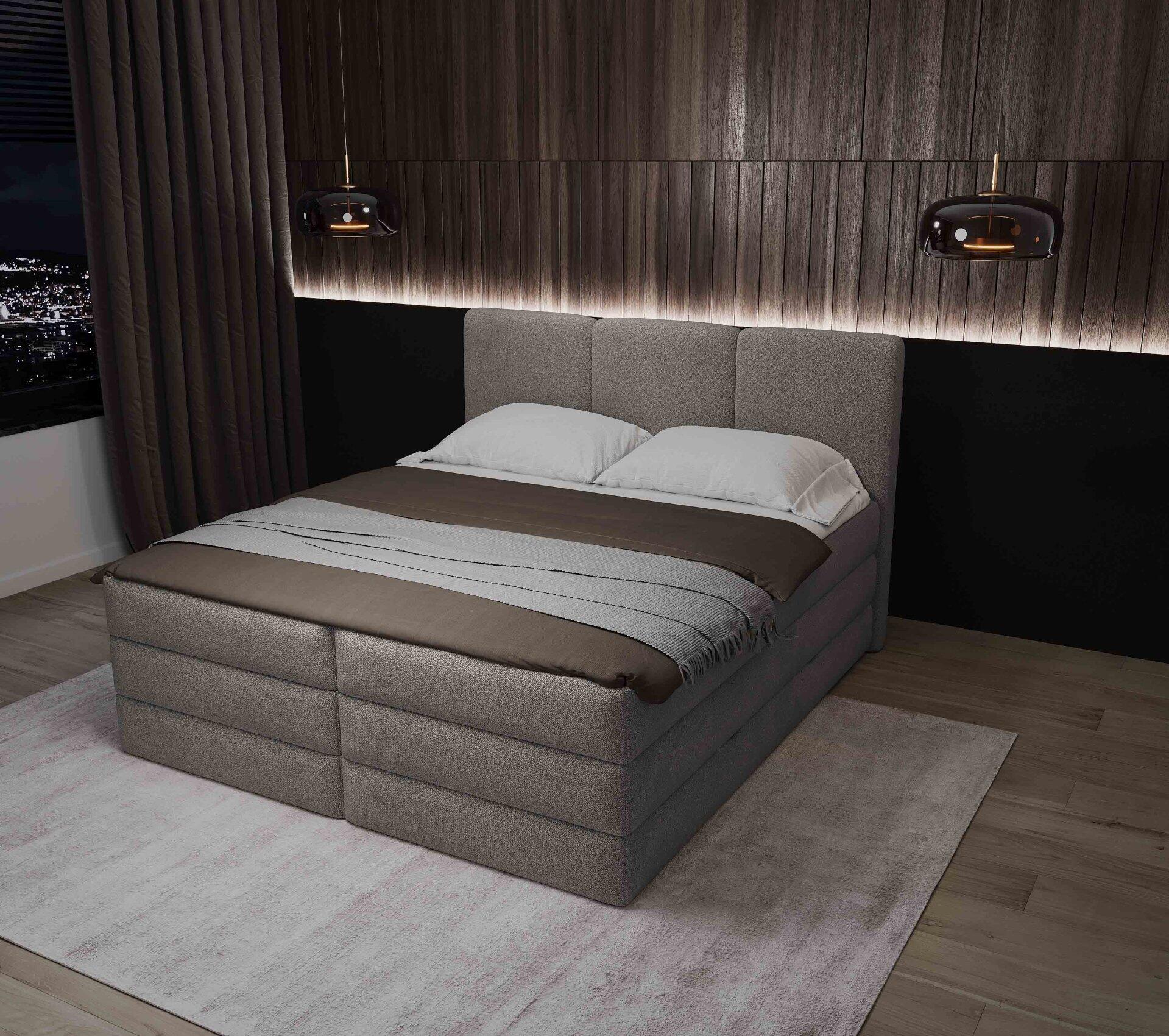 Breites Boxspringbett Castel mit grauem Stoffbezug, gestepptem Kopfteil und vertikalen Feldern, eingebettet in ein stilvolles Schlafzimmer mit Wandverkleidung und Beleuchtung.