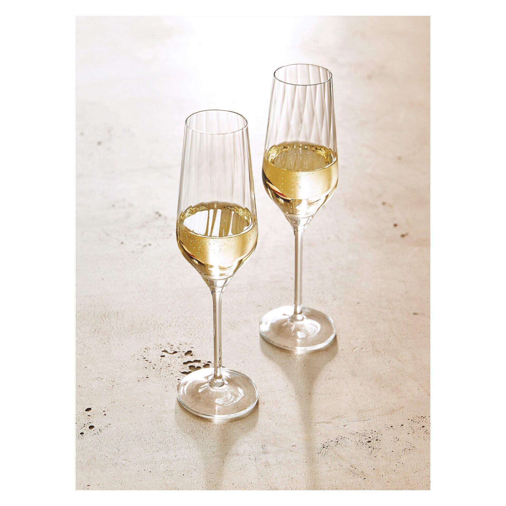 Zwei elegante Champagnergläser mit Reliefstruktur, zur Hälfte mit einem perlenden Getränk gefüllt, auf einem hellen Untergrund.