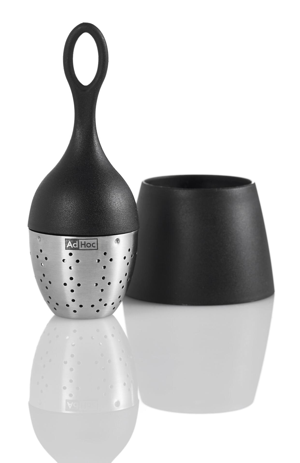 Teekorb Floatea aus Edelstahl mit feinmaschigem Gitter und schwarzem Griff, zusammen mit einer schwarzen Tasse auf weißem Untergrund.