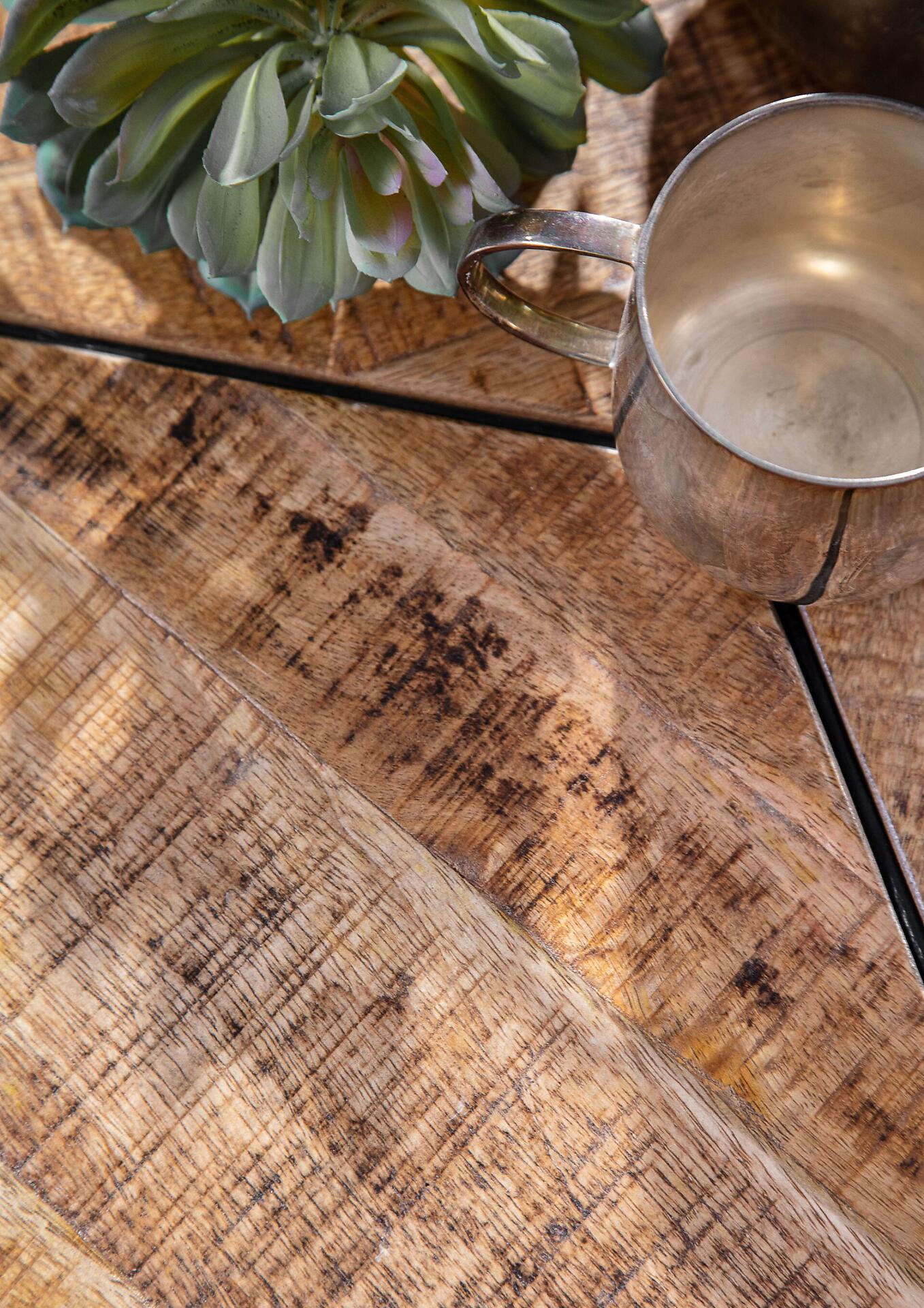 Rustikaler Holztisch mit schwarzen Metallfüßen, aus einer Vogelperspektive, zeigt Maserung und Unebenheiten des Holzes sowie eine dekorative Sukkulente und einen silberfarbenen Becher.