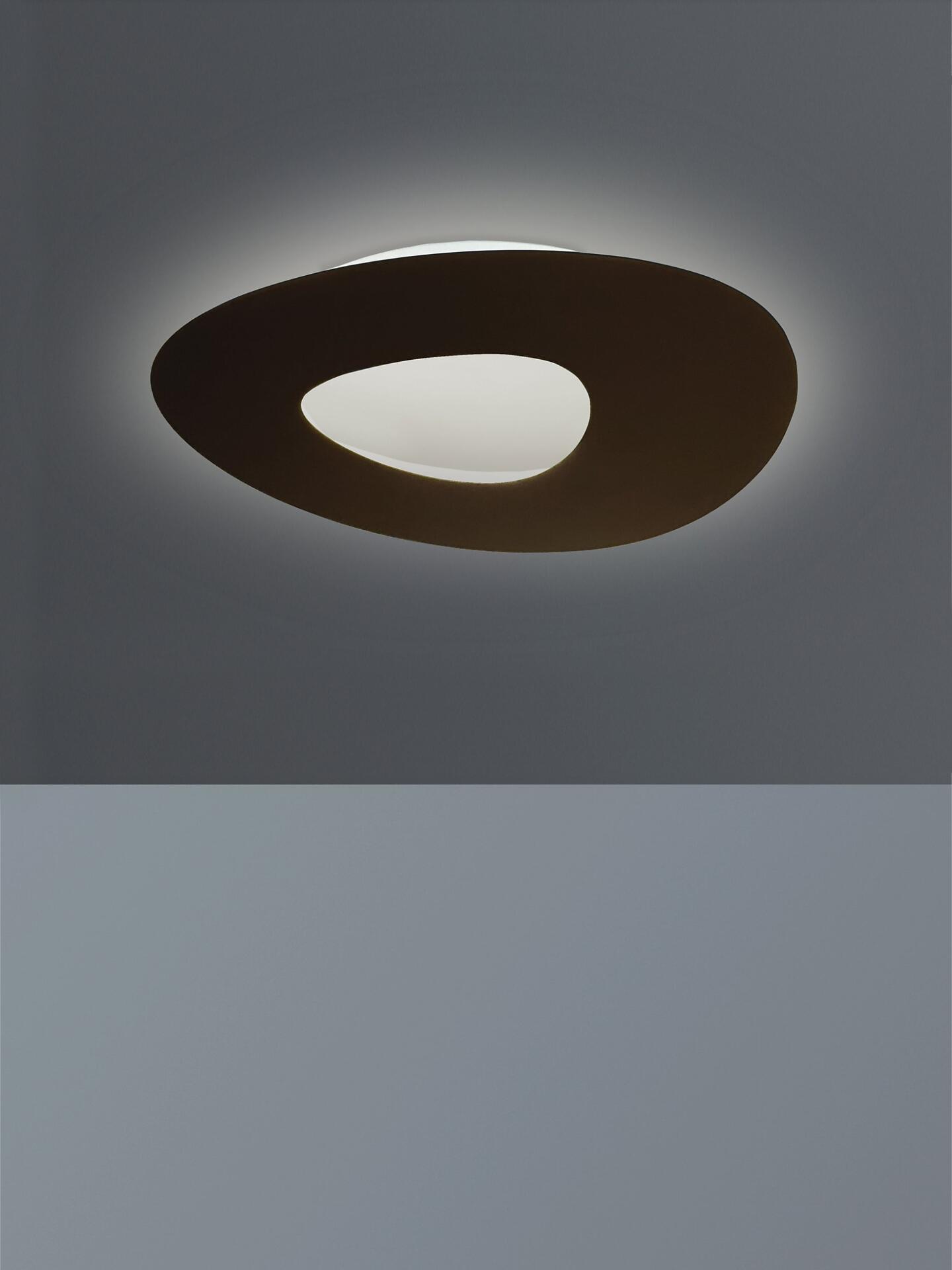 Deckenleuchte Drill, eine runde, oval geformte Leuchte mit dunklem Außenelement und weißem Innenraum, die ein warmweißes Licht gleichmäßig abstrahlt.